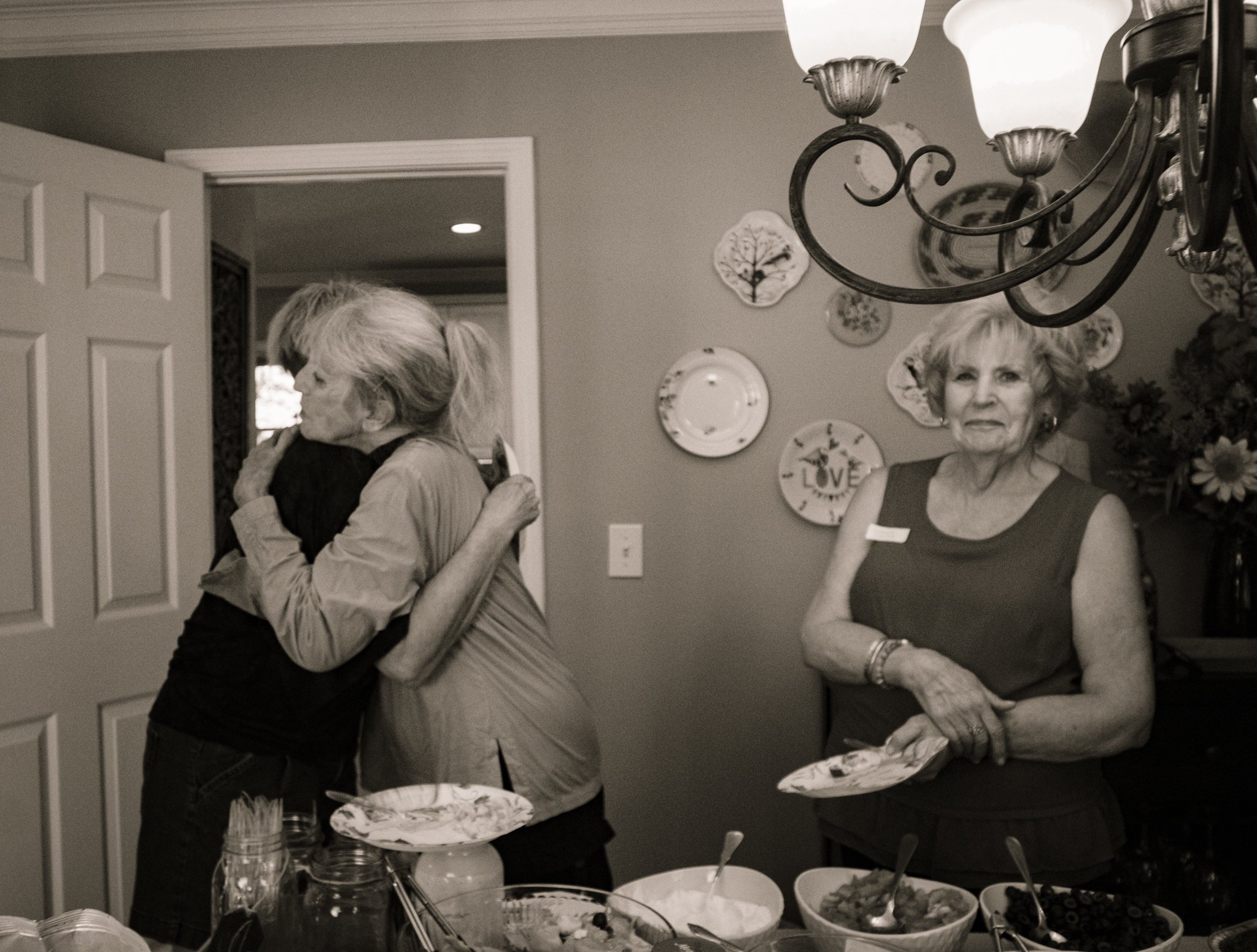 Two women hugging at a gathering in a decorated dining room.