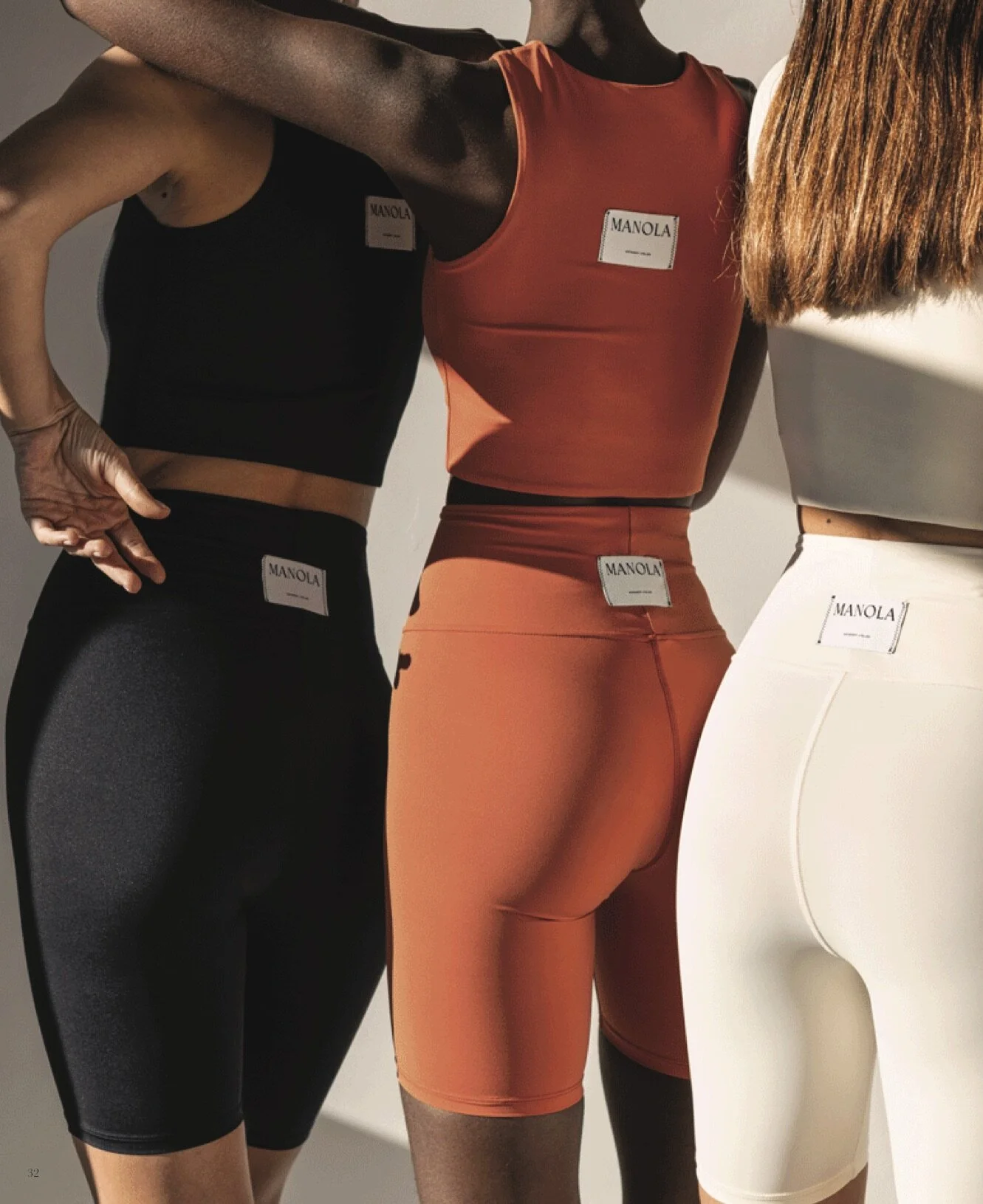 Three mannequins wearing athletic clothing, including a black sports bra and leggings, an orange sports top and leggings, and a white sports bra and leggings, all with tags that say 'MANOLA'.