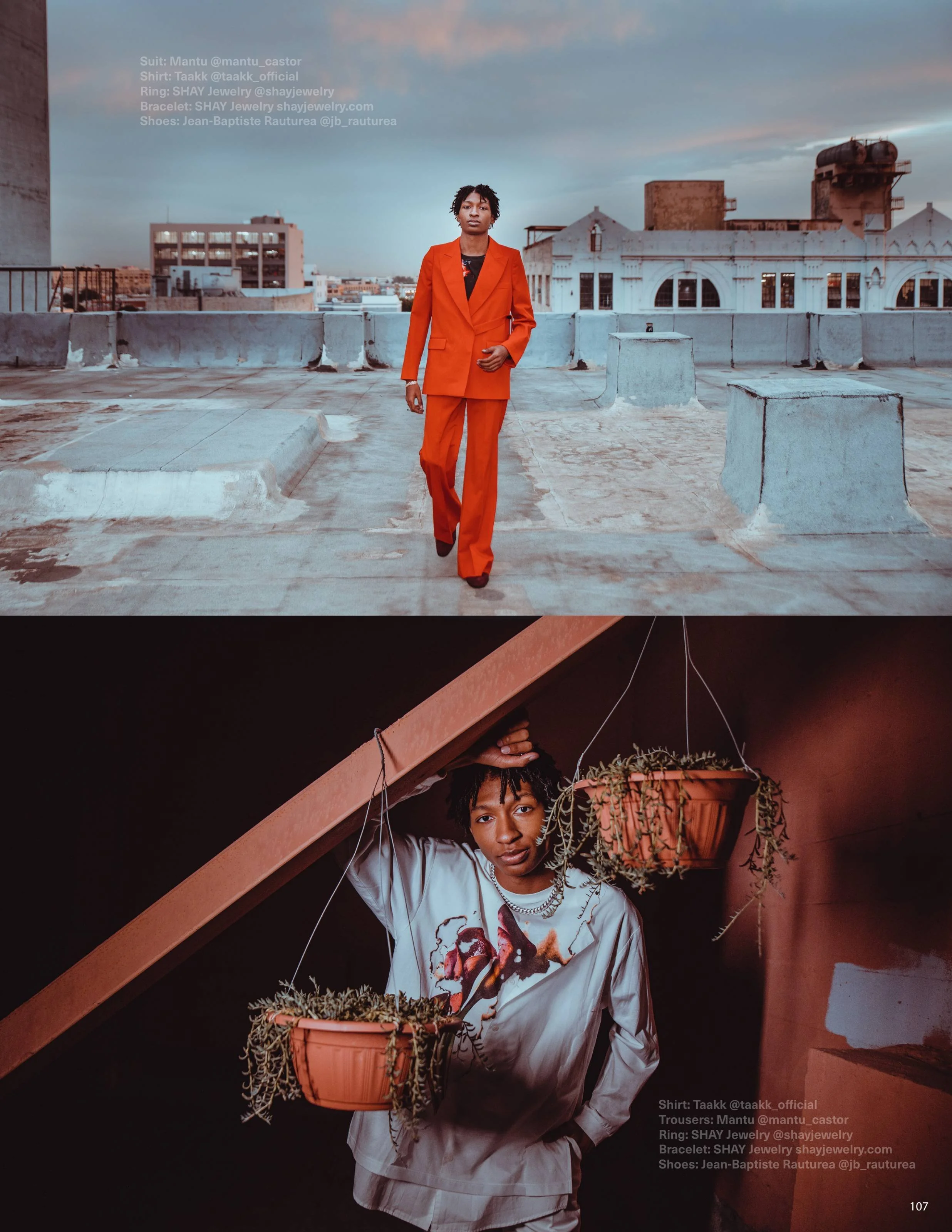 A person in an orange suit and matching pants standing on a rooftop against a cityscape at dusk, with light reflecting off the buildings. The individual has short, curly hair and a serious expression.