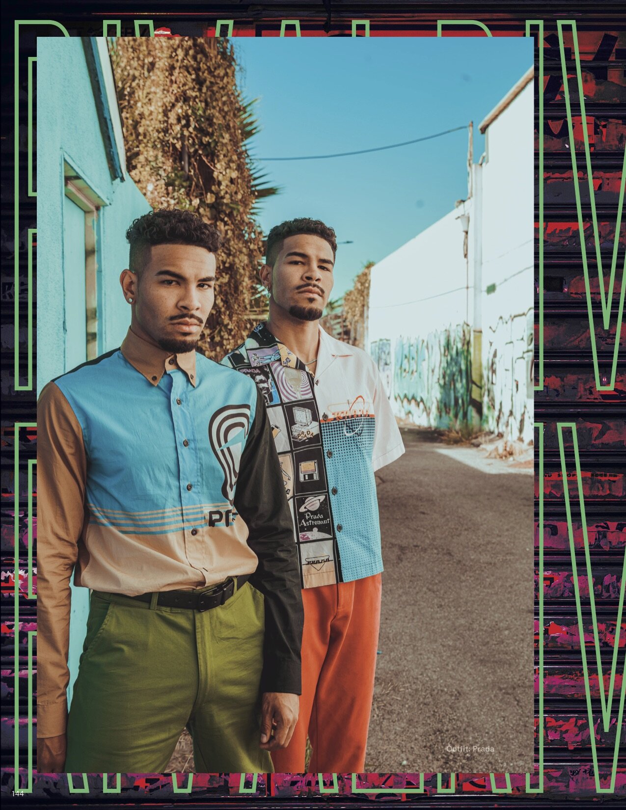Two young men standing outdoors beside a vibrant, graffiti-covered wall, wearing colorful Prada outfits against a sunny, clear sky.