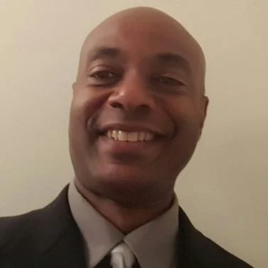 A man smiling in a suit and tie.