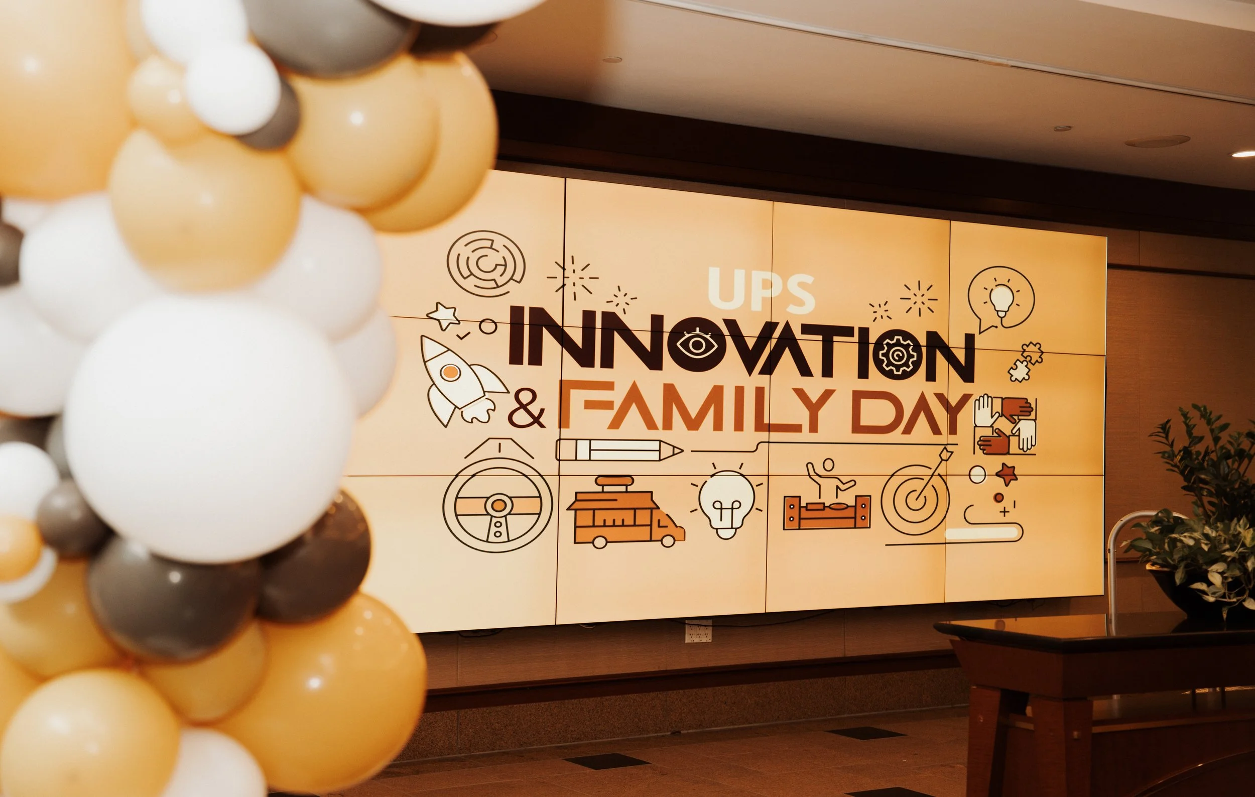 Decorative balloon display in front of a large sign for UPS Innovation & Family Day event. The sign features various icons related to ideas, creativity, and teamwork.