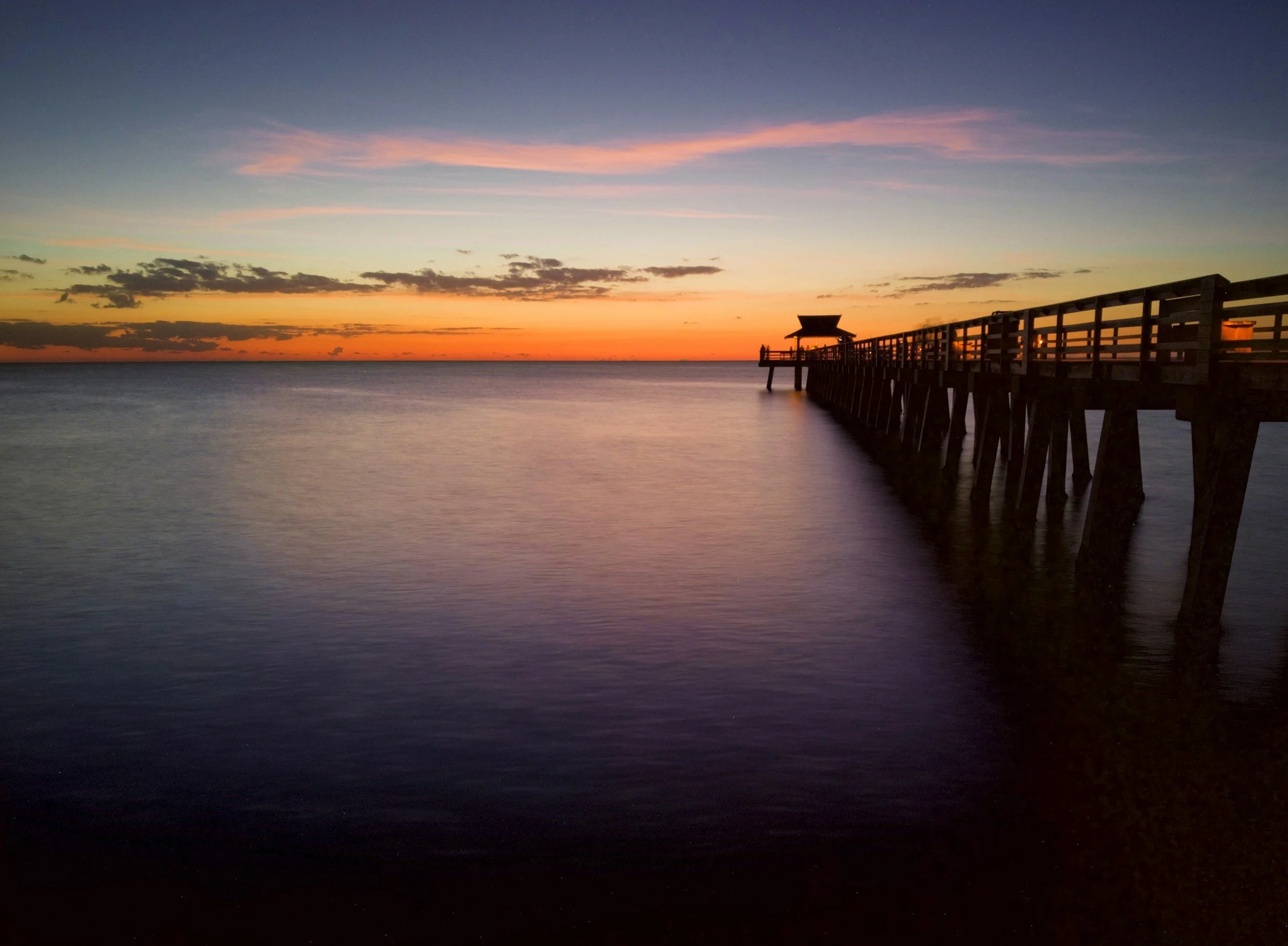 Calm ocean waves and pastel sunset horizon along the Gulf of Mexico coast in Naples, Florida