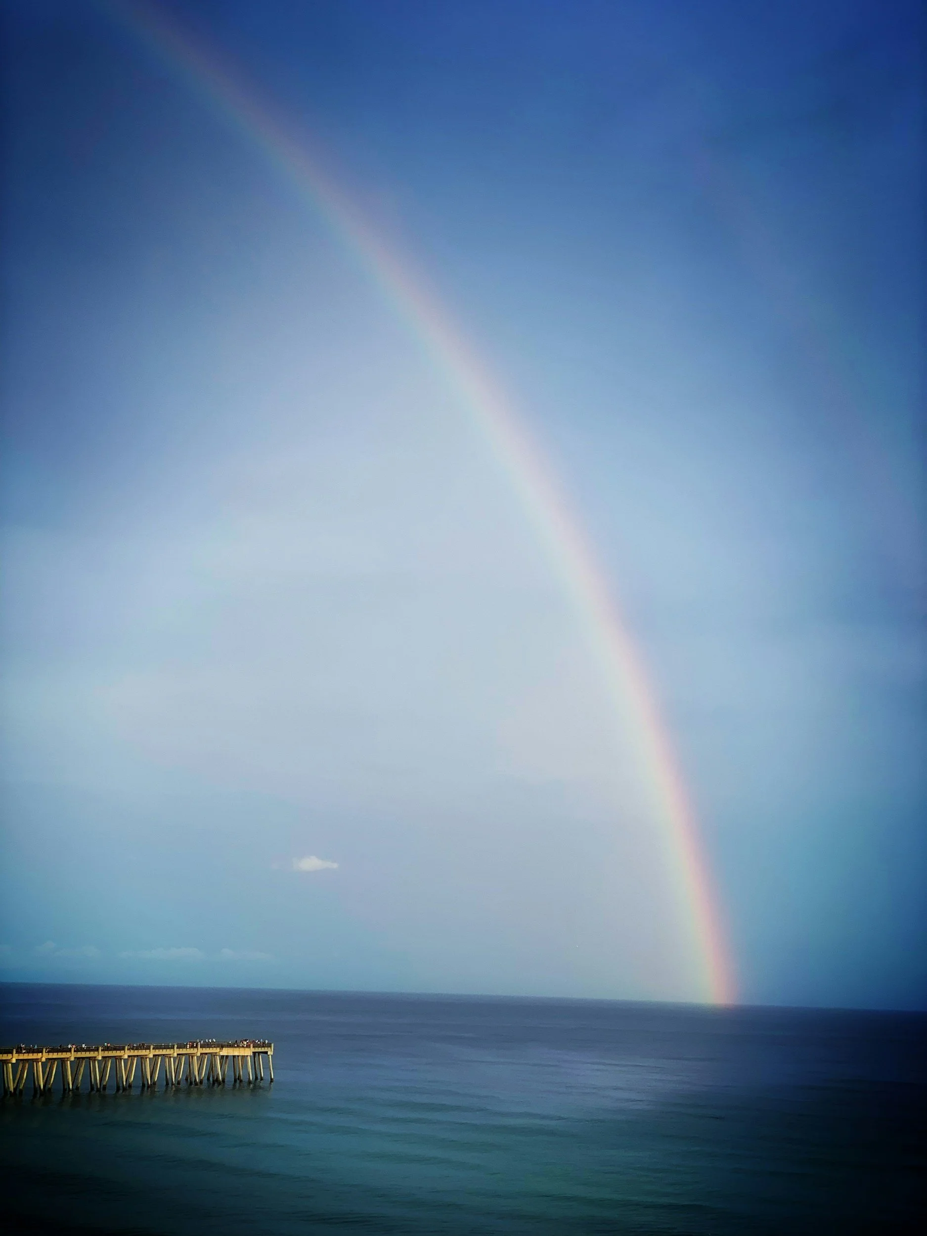oft rainbow light refraction reflecting across calm turquoise ocean waters along a Naples beach