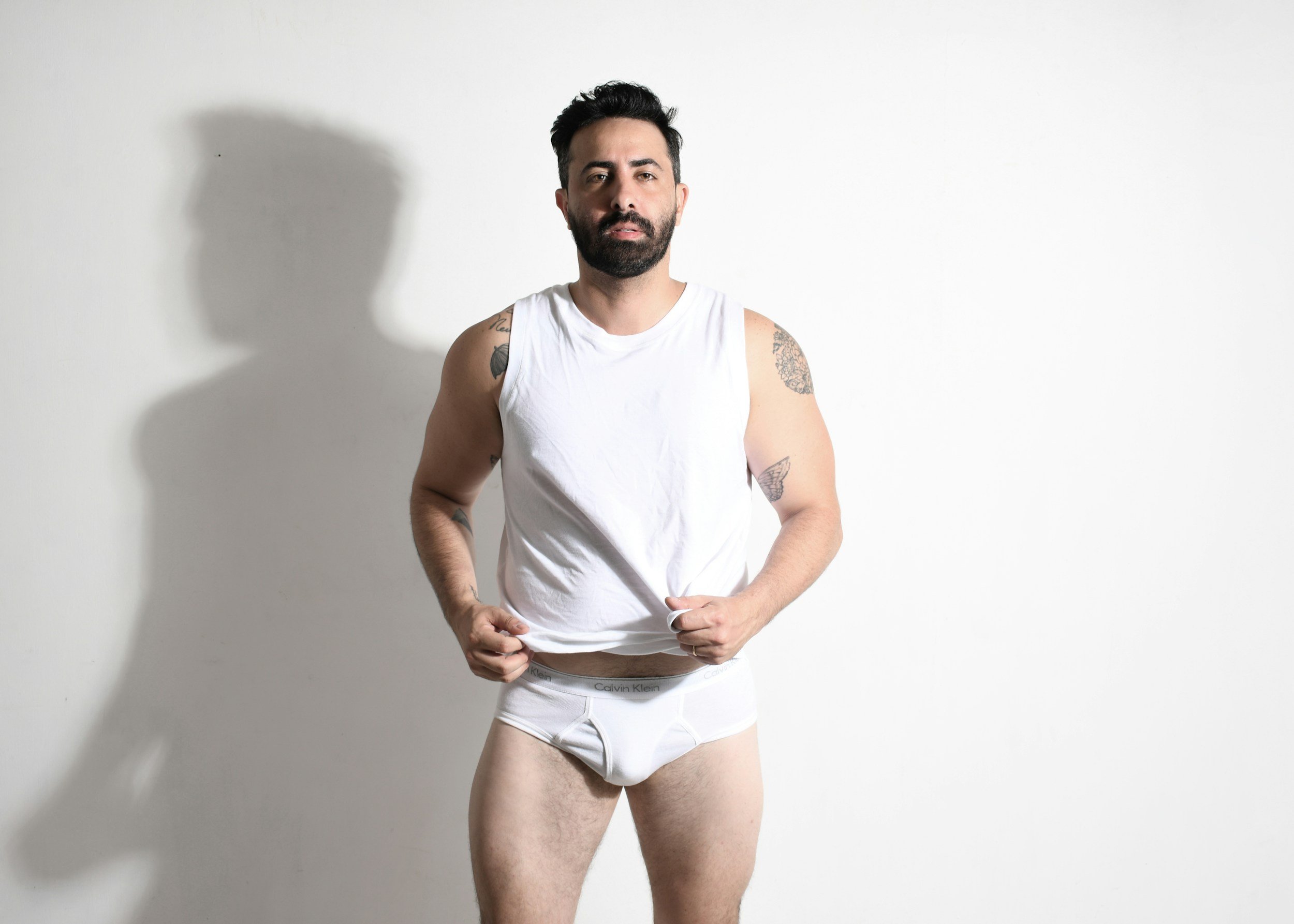Tattooed man posing in a white tank top, featured on Calming Tides Therapy's queer and sex-positive service page.