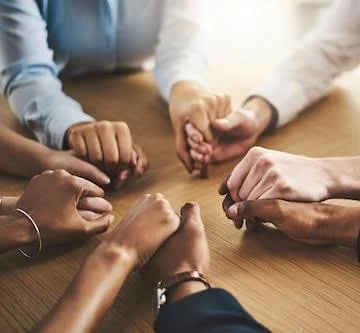 Group of diverse hands joined together over a wooden table during a supportive group therapy session