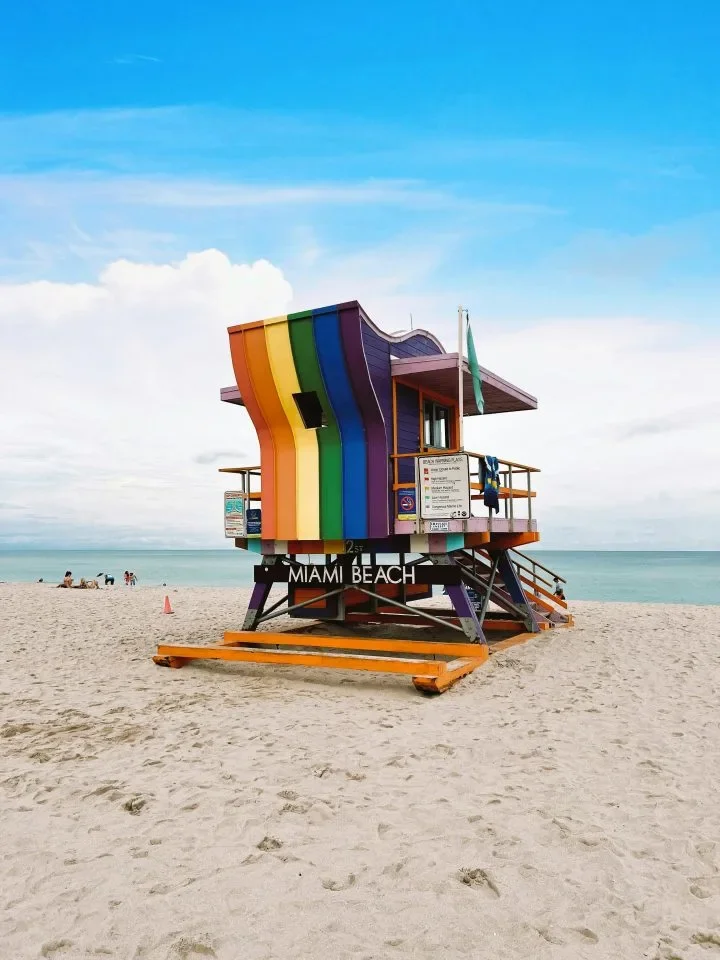 A rainbow-painted Miami Beach lifeguard tower on a sandy beach, symbolizing a safe haven and LGBTQ+ inclusive care.