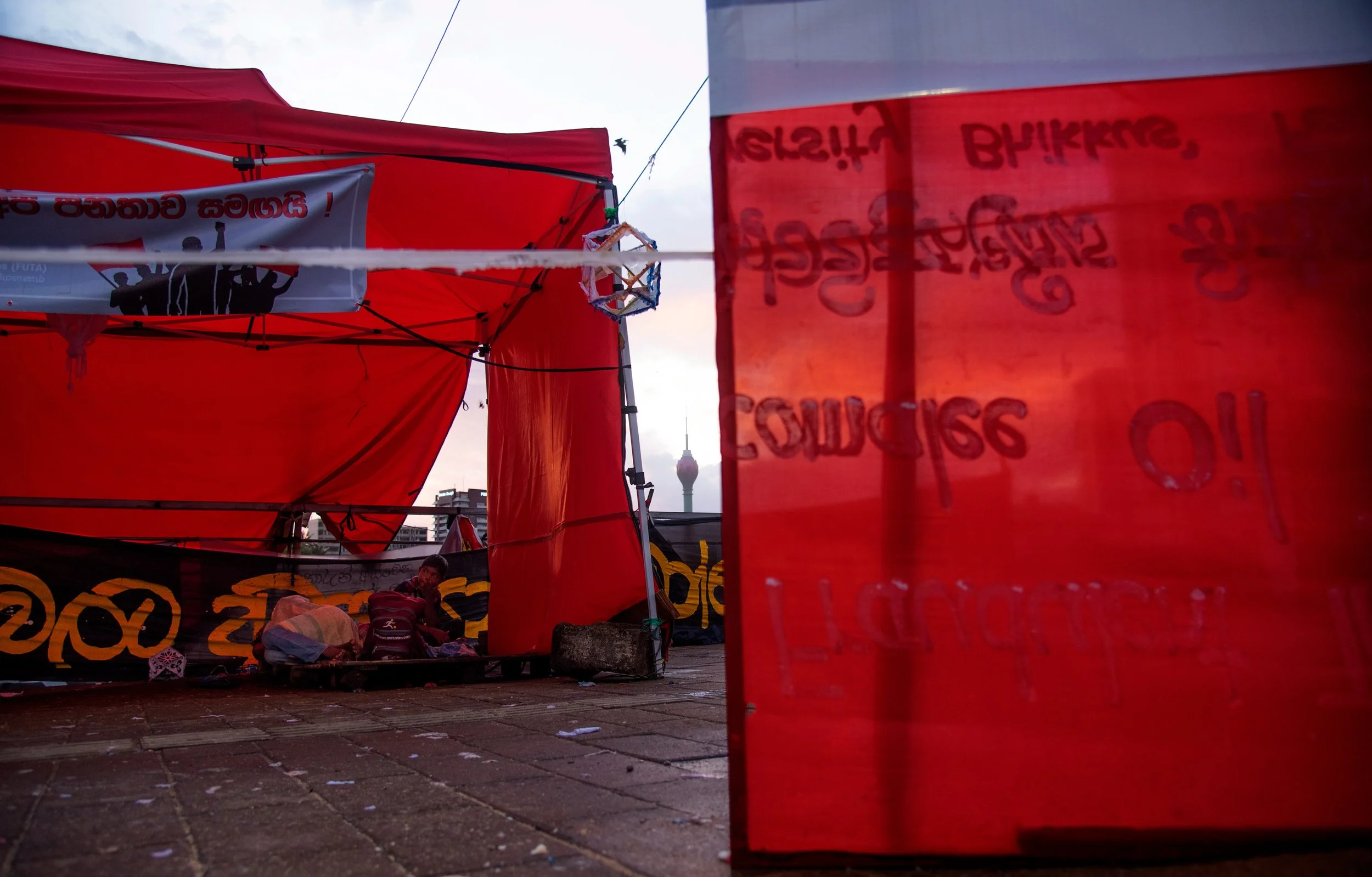 At nearly 5:00 a.m. on August 23, 2023, following a Vesak night marked by heavy rain and strong winds, at Gota Go Gama in Galle Face, Colombo...  Through the mist, past the remnants of shattered university students' protest tents and broken Vesak lan