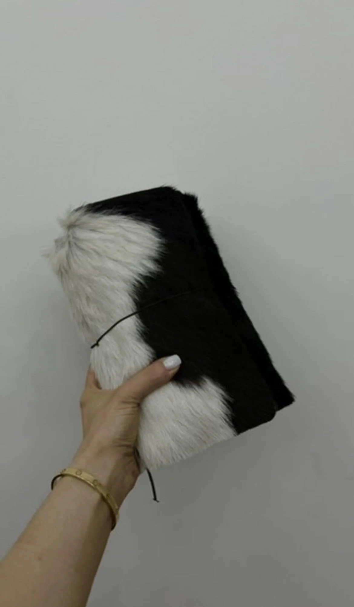 A person holding a rectangular notebook with a black and white fur pattern cover, against a plain gray wall background.