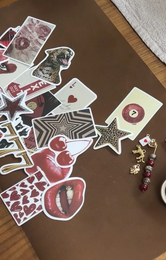 A collection of various decorative stickers and jewelry items arranged on a brown surface, including lips, a star, a leopard face, cherries, dice, a heart, and some charms.