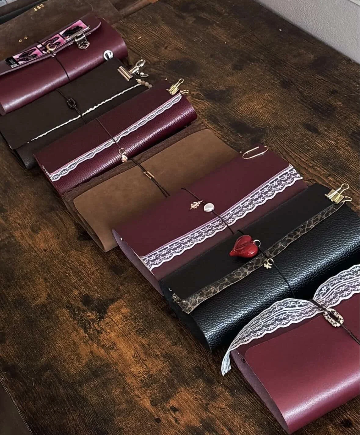 A collection of notebooks with decorative trims and accessories, arranged on a wooden surface.