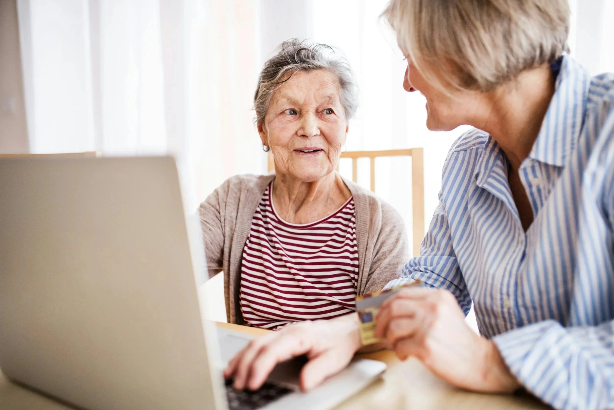 An older woman and a younger woman collaborate on a laptop, sharing ideas and engaging in conversation.