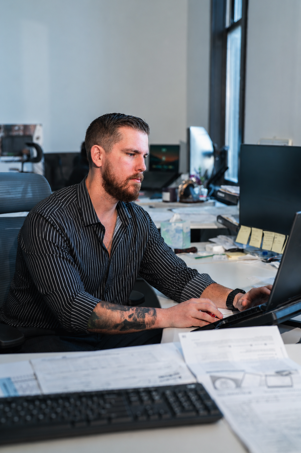 Man working at a desk in an office, looking at a laptop.