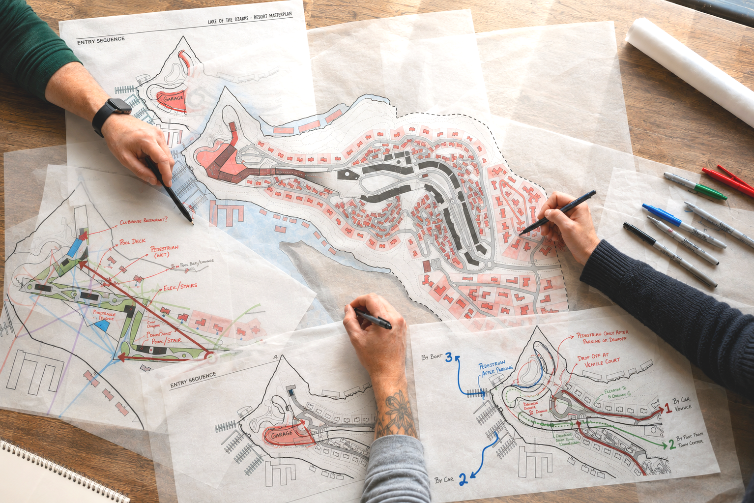 People working on multiple detailed master plan drawings for a resort, including roads, buildings, and landscape features on a large table with markers and pens nearby.