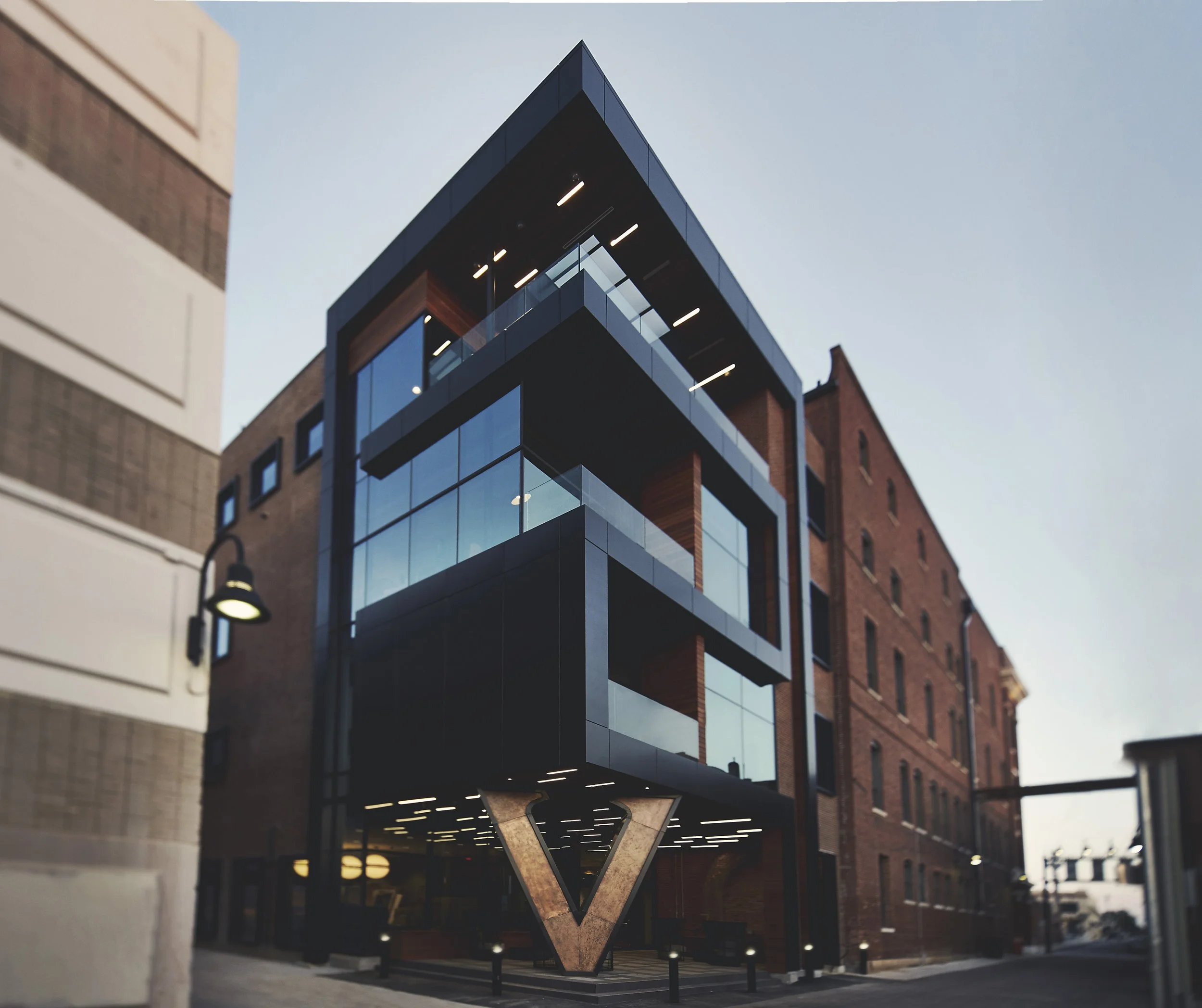 Modern building with glass balcony and geometric design, above a brick building, during dusk or early evening.