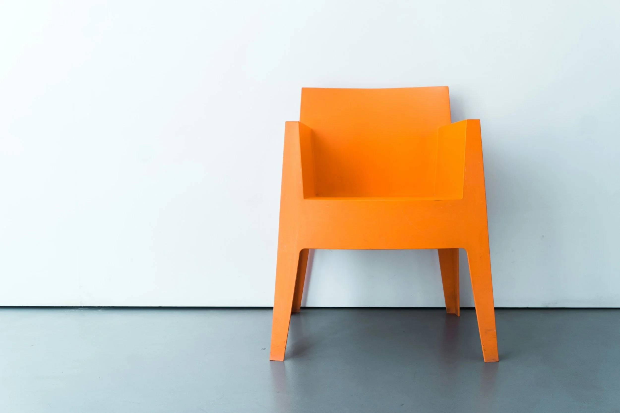 An orange chair positioned against a white wall with a light blue floor.