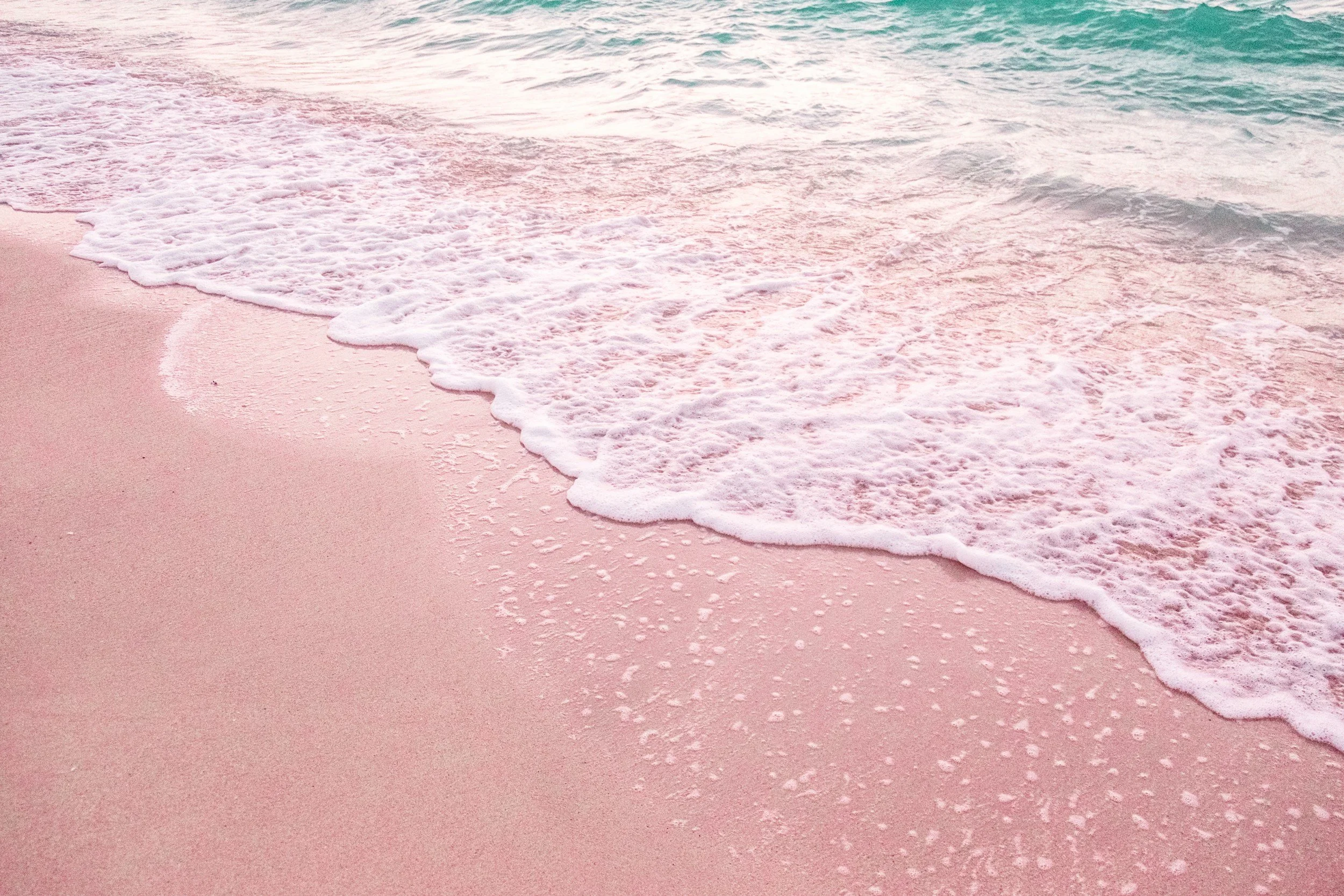 Pink sandy beach with waves gently washing ashore.