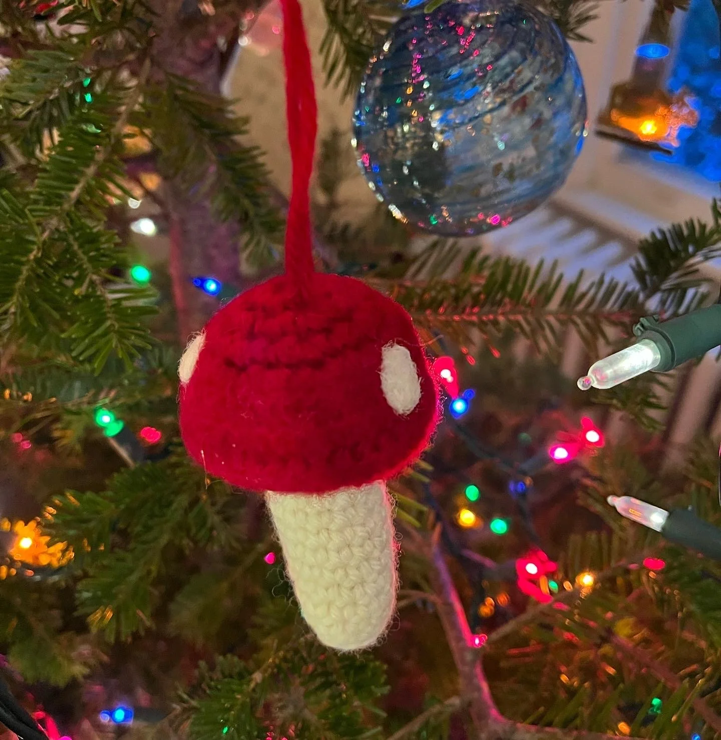 A Christmas tree decorated with colorful lights, a red and white sock ornament, and a blue glass ball ornament.