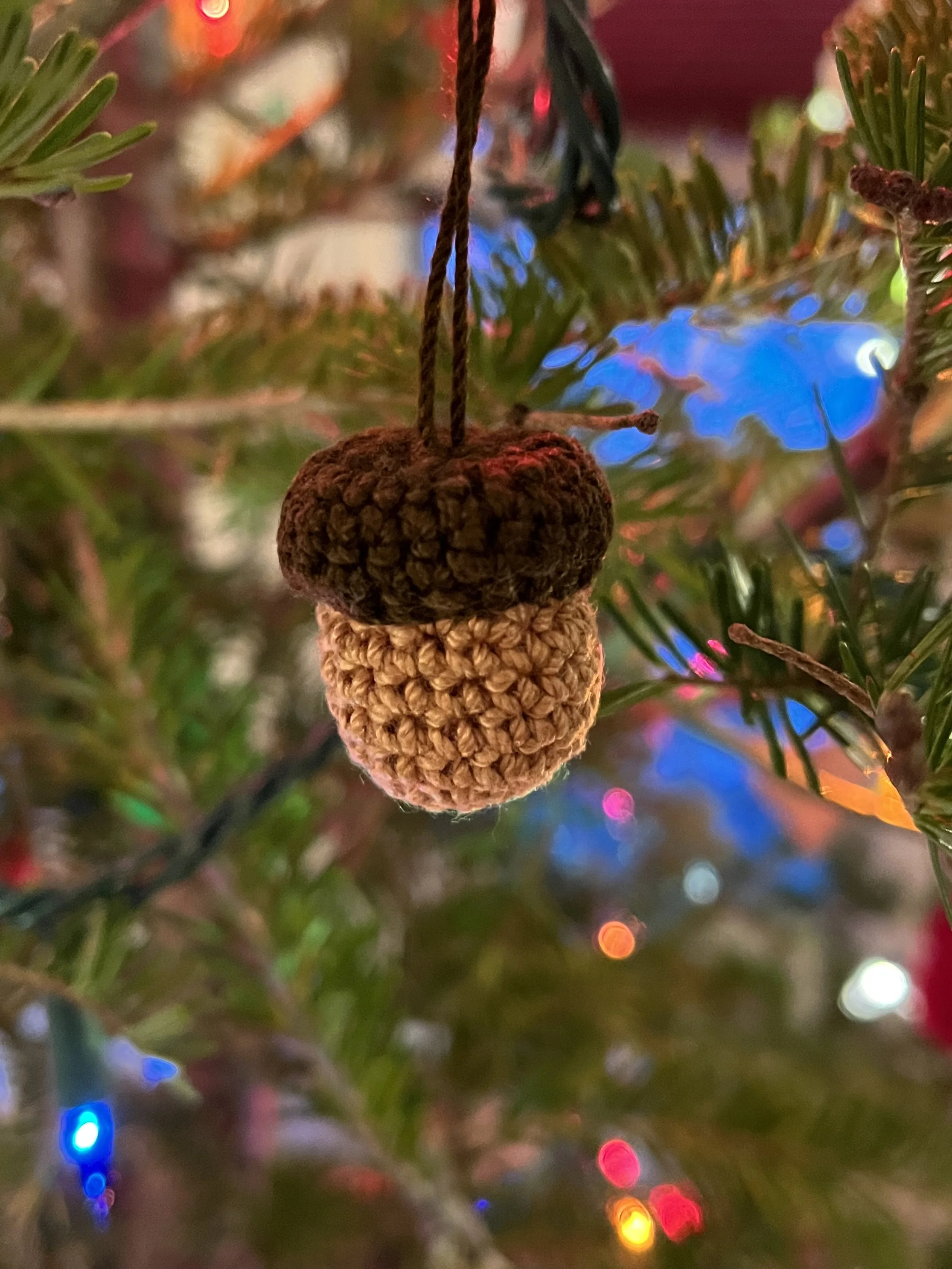 Close-up of a crocheted Christmas tree ornament hanging on a decorated Christmas tree with multicolored lights.