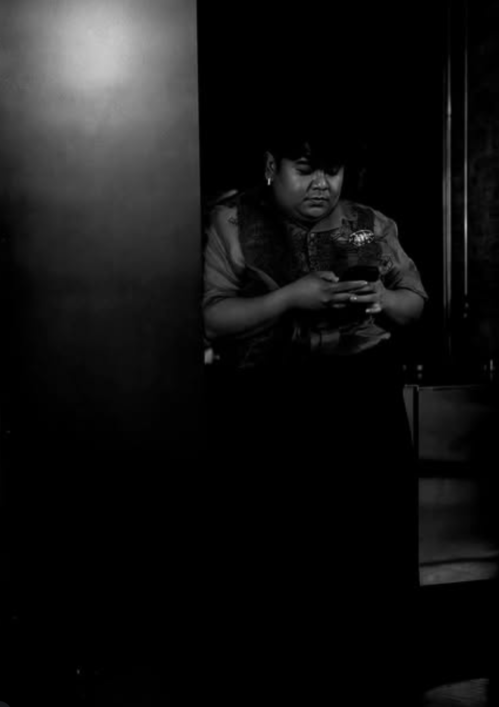 Woman looking at her phone in a dimly lit space, partially obscured by a wall or door