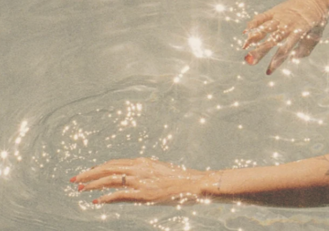 Hands touching water with sunlight reflections and sparkles.