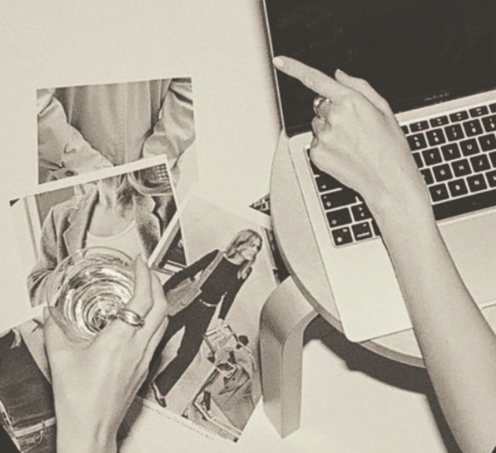 Person using a laptop with photographs on the table, one holding a glass of water.