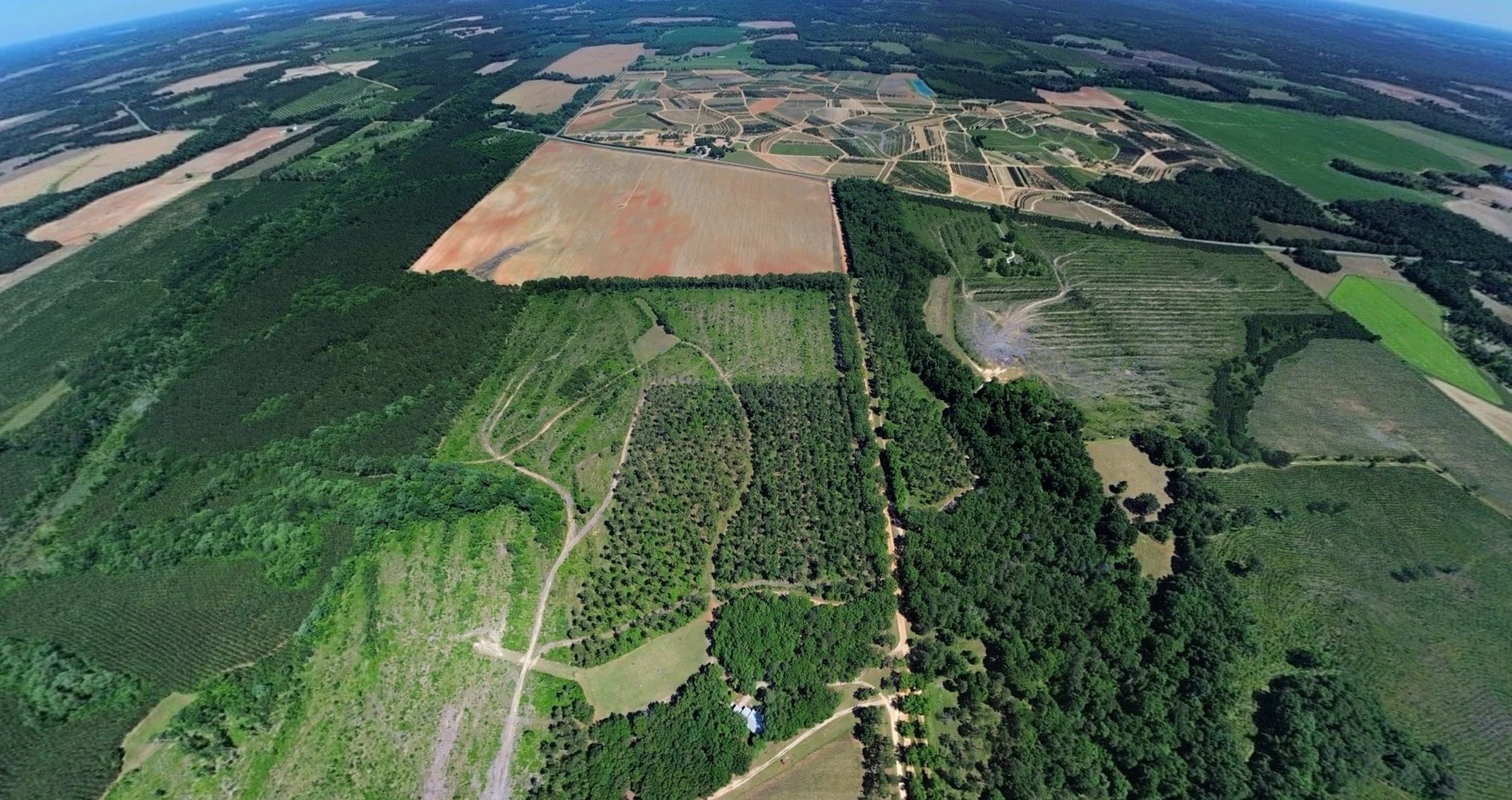 Aerial view of farmland with forests, fields, and roads in a rural area.