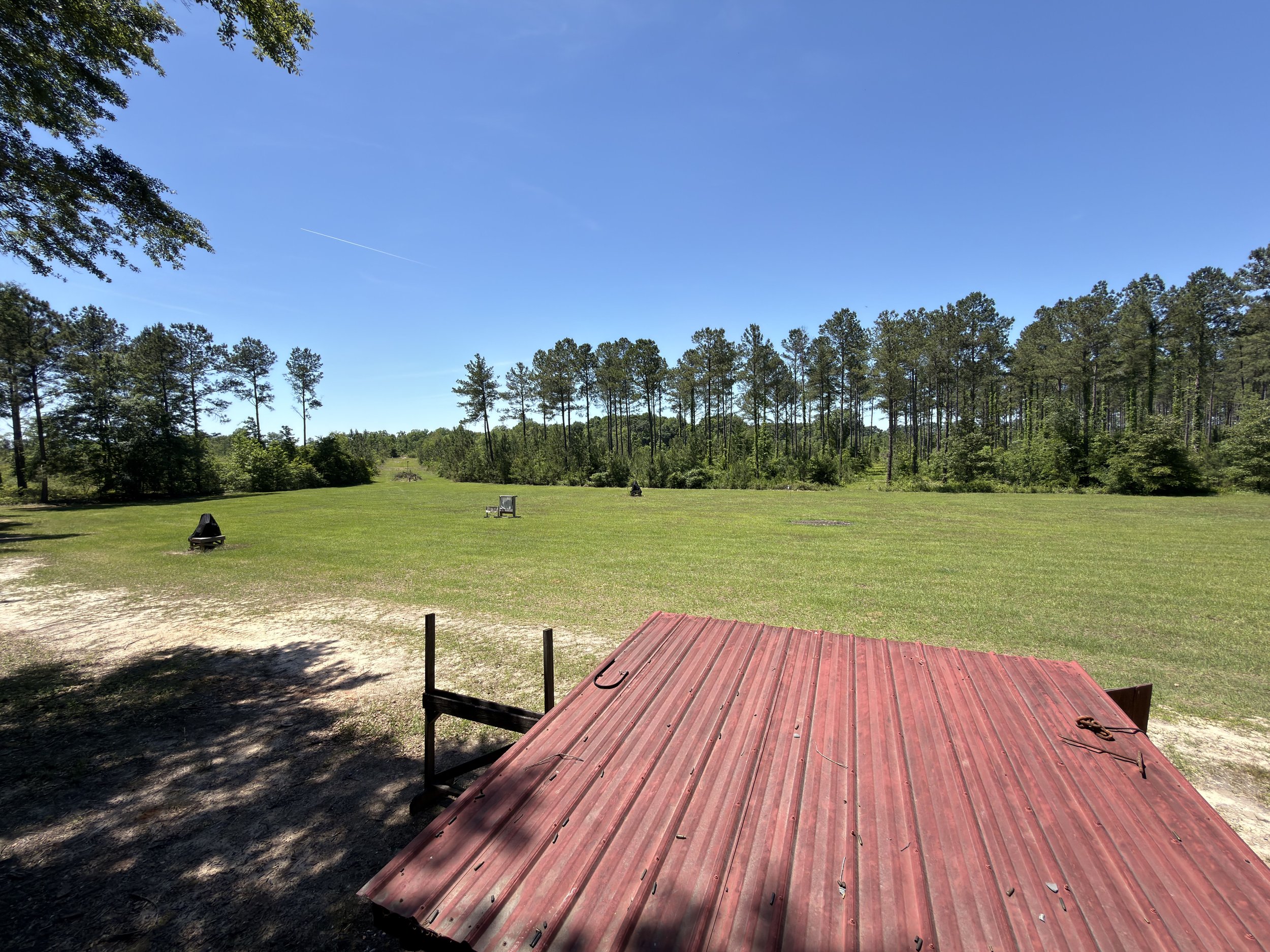 Open grassy field with trees and clear blue sky, with a red roofed structure in the foreground.