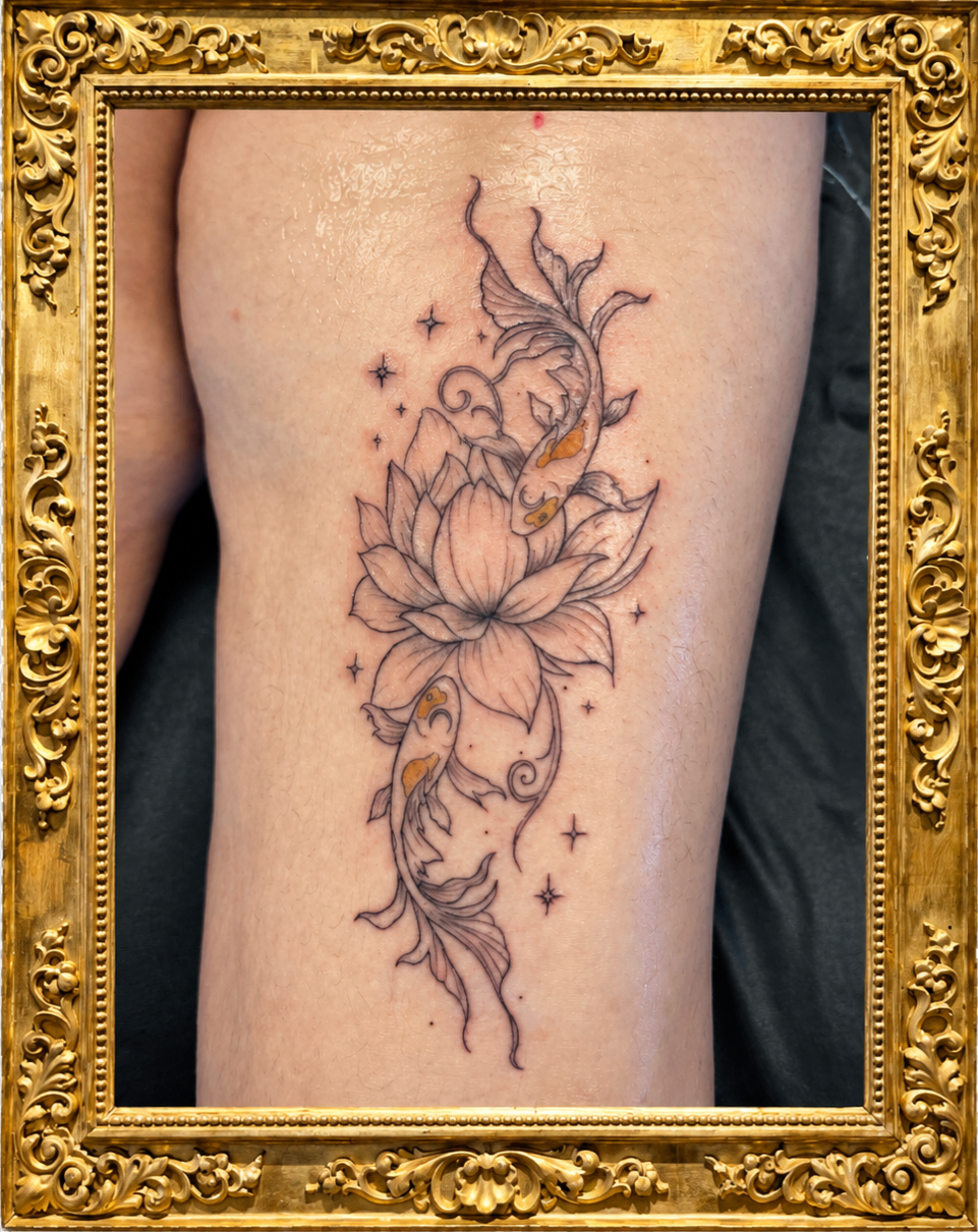 A tattoo of a lotus flower with flowing, whimsical lines, surrounded by small stars and two koi fish swimming around it, on a person's thigh, framed with an ornate gold frame.