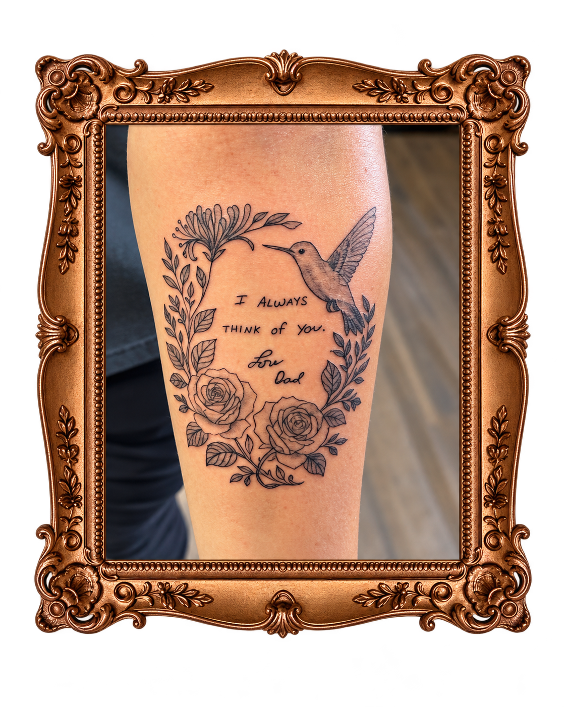 Tattoo of a hummingbird, roses, and leaves with the handwritten message "I always think of you. Love Dad" on a person's arm, framed by an ornate gold picture frame.