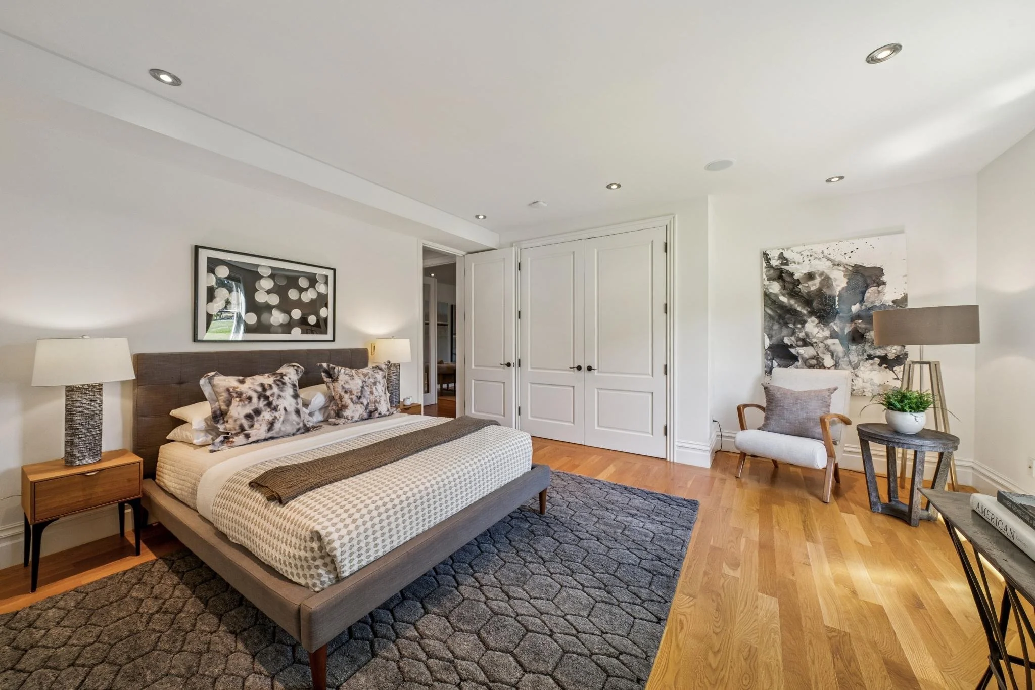 A bedroom with a bed, bedside tables with lamps, and modern artwork on the white walls.