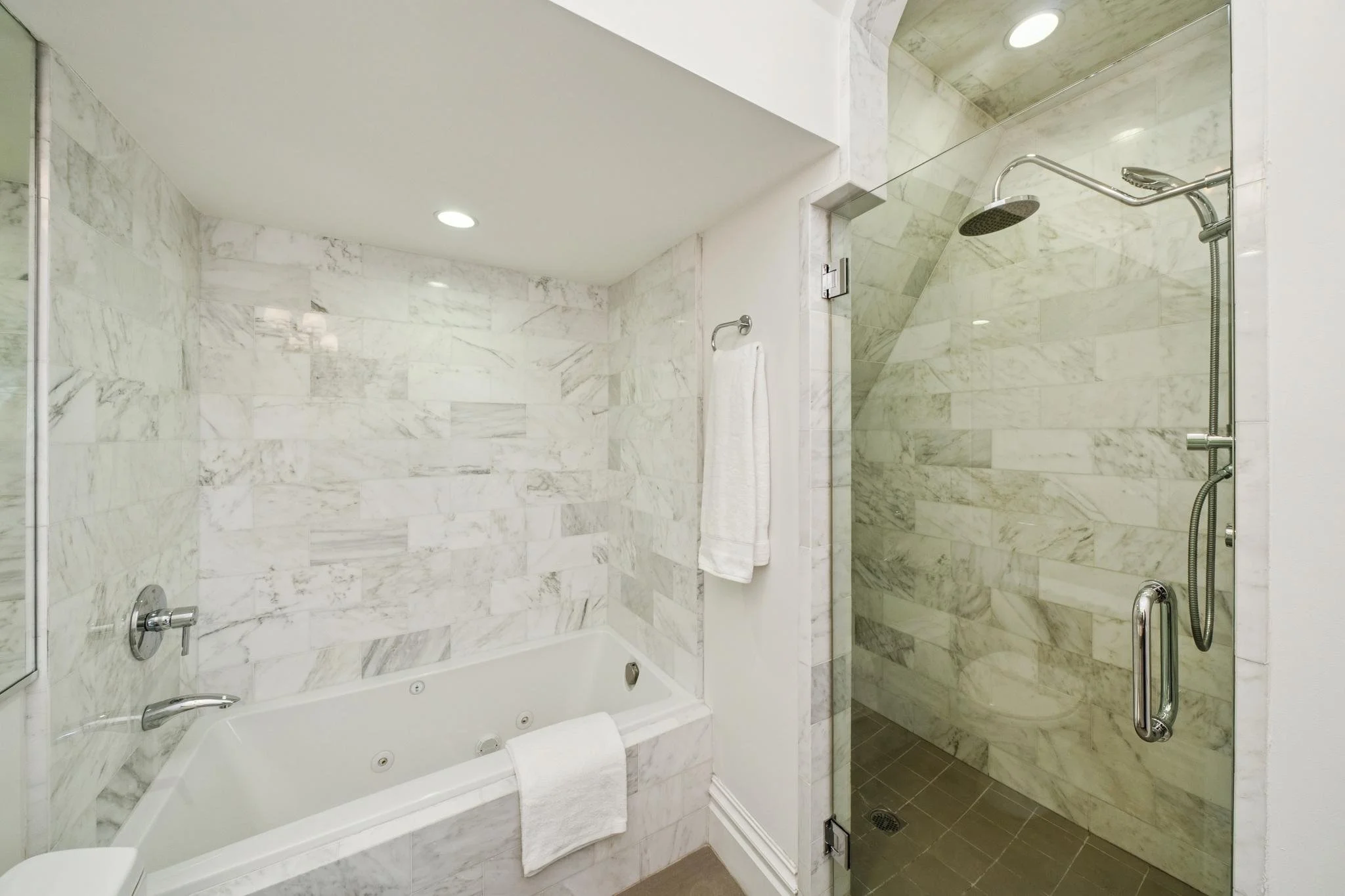 A luxurious marble bathroom with a built-in bathtub and a separate walk-in shower area, featuring a ceiling light and modern fixtures.