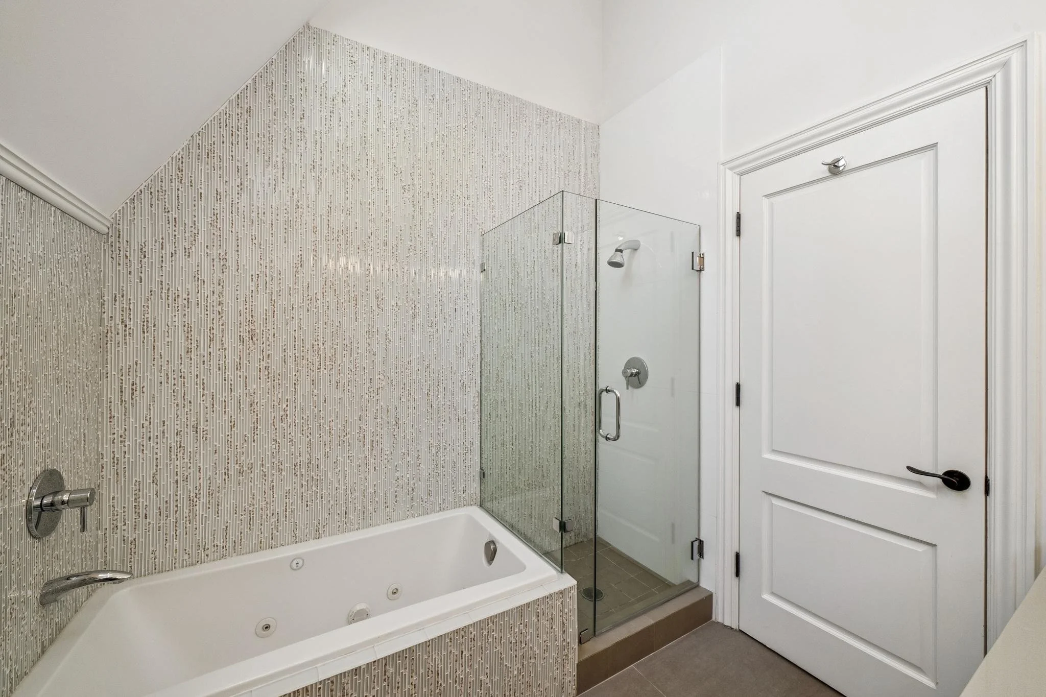 Bathroom with a bathtub, a glass shower enclosure, and a white door with decorative trim.