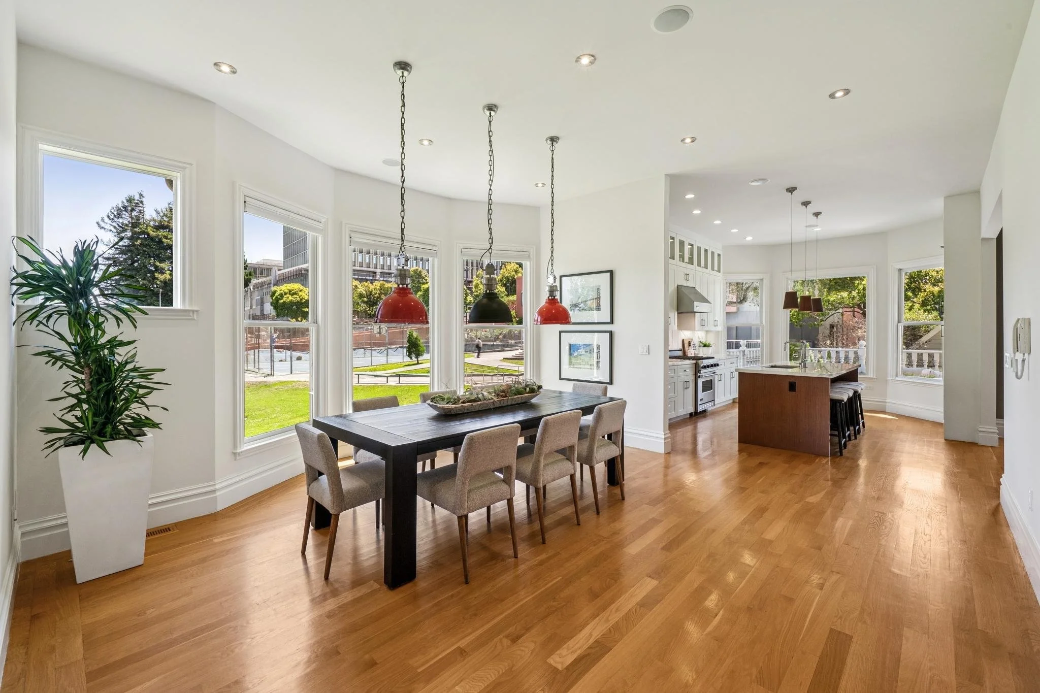 Bright, modern kitchen and dining area with large windows, wooden floor, and pendant lights over the dining table.