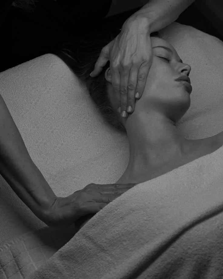 A person receiving a massage, lying on a massage table with their eyes closed, while the masseuse's hands apply pressure to their neck and head in a calming scene.