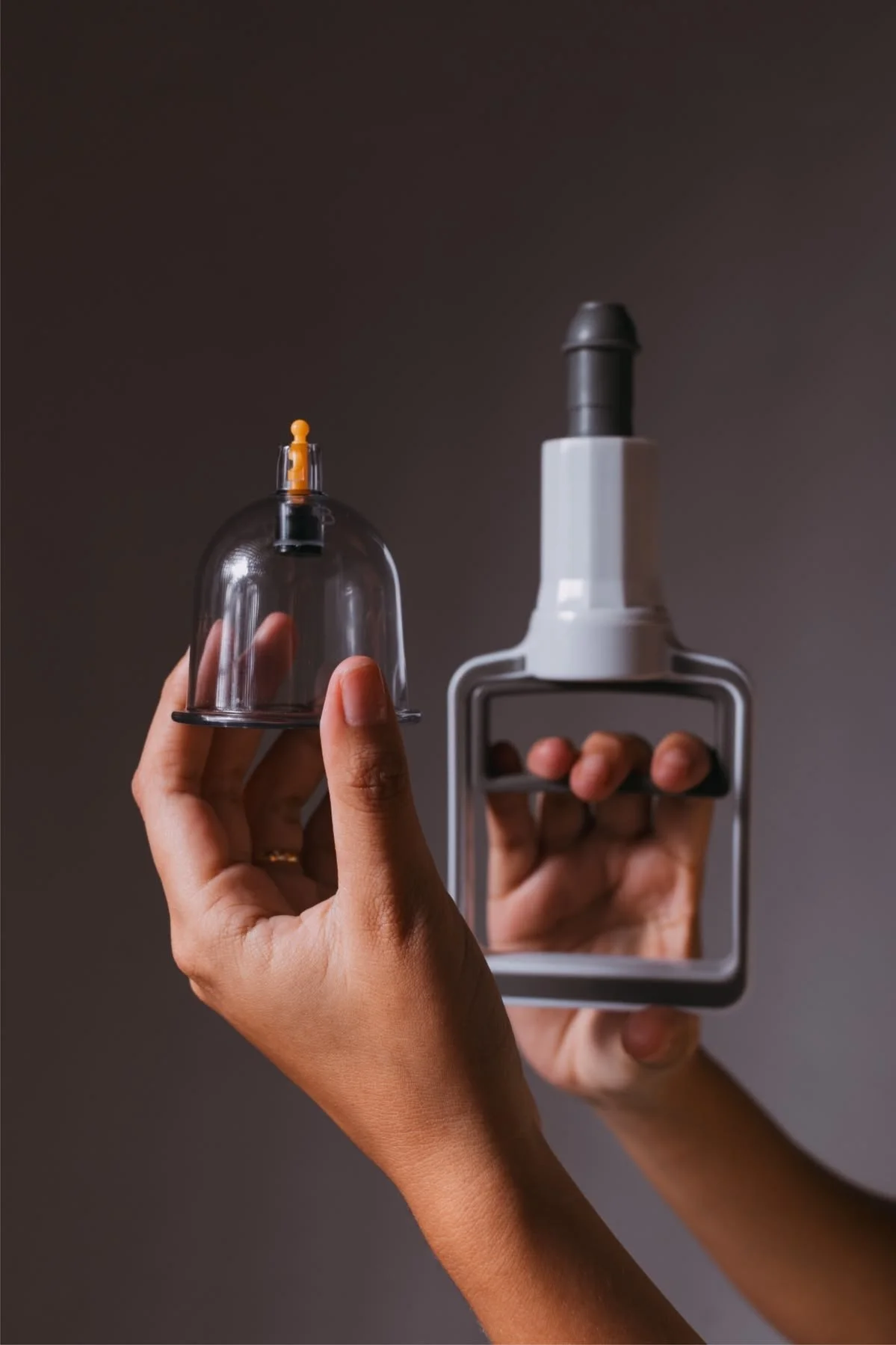 Two hands holding a glass bell jar and a small extinguisher, with a dark gray background.