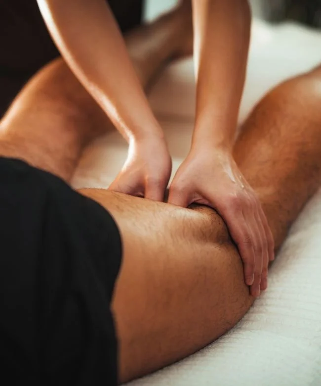 Person receiving a massage on their thigh by another person in a black shirt.