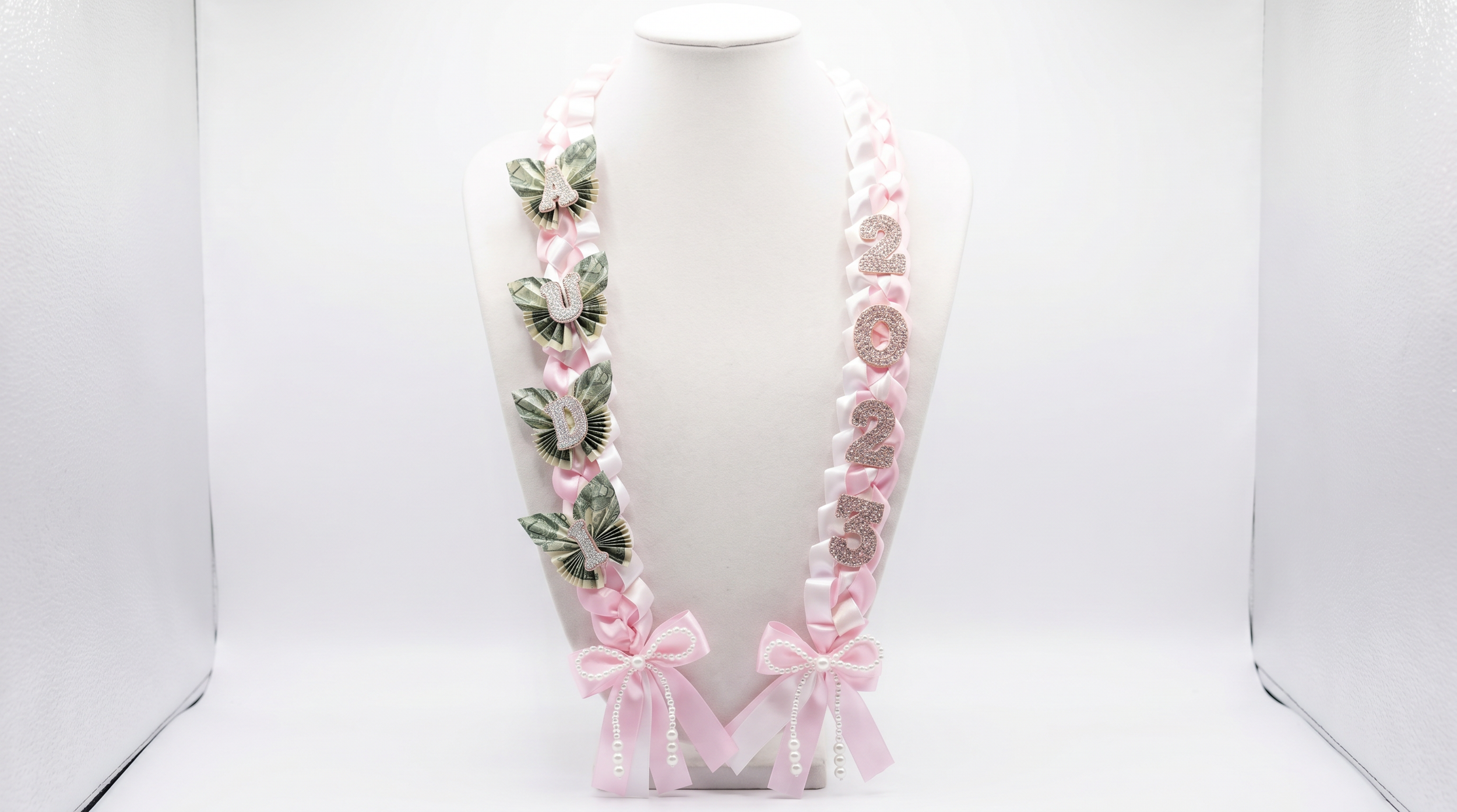 Pink and white ribbon garland with glittery numbers and bows on a white display stand. corpus christi Custom graduation gifts, lei