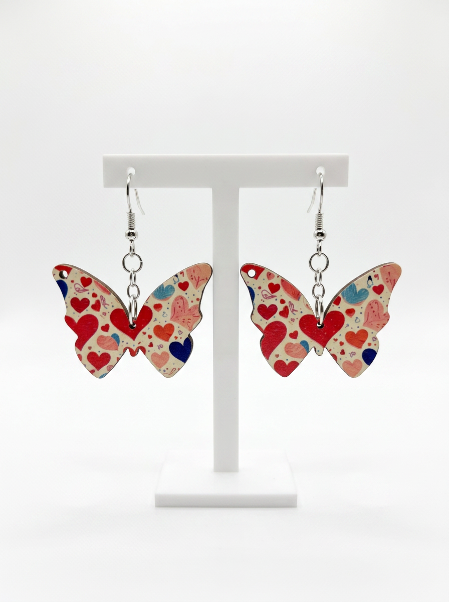 Butterfly-shaped earrings with red, pink, blue, and beige heart patterns displayed on a white stand.