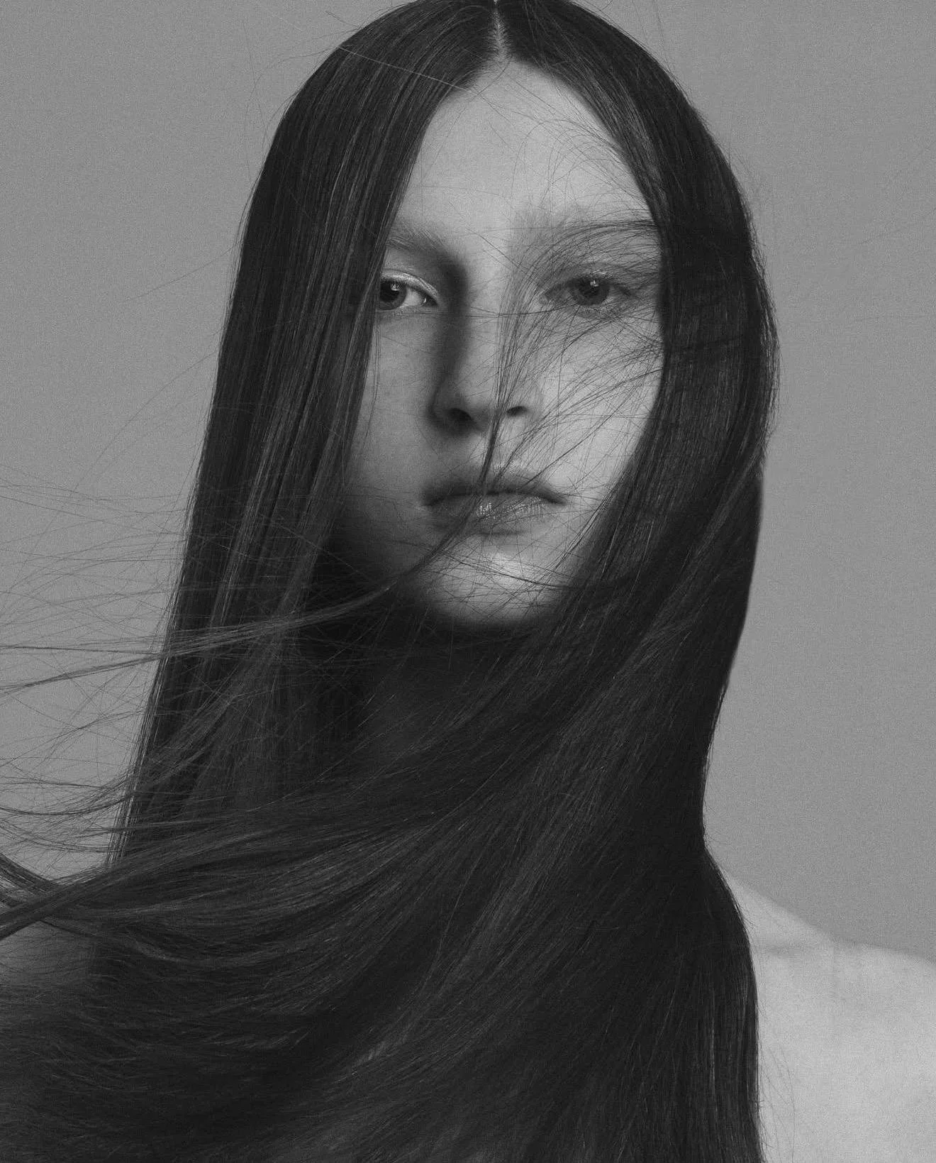 Black and white portrait of a woman with long, flowing hair covering part of her face, looking directly at the camera.