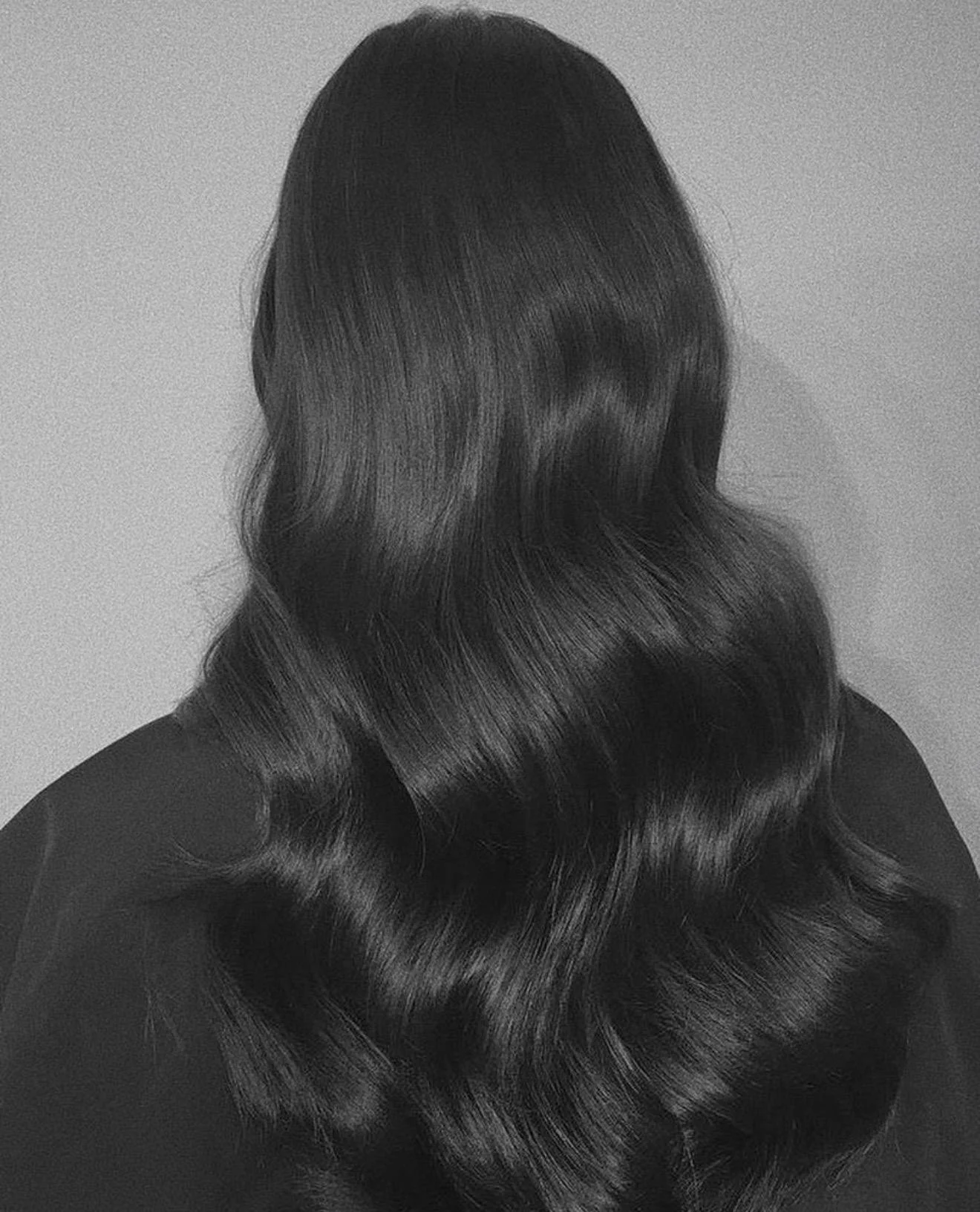 Black and white photograph of a woman with long, wavy, shiny hair viewed from the back.
