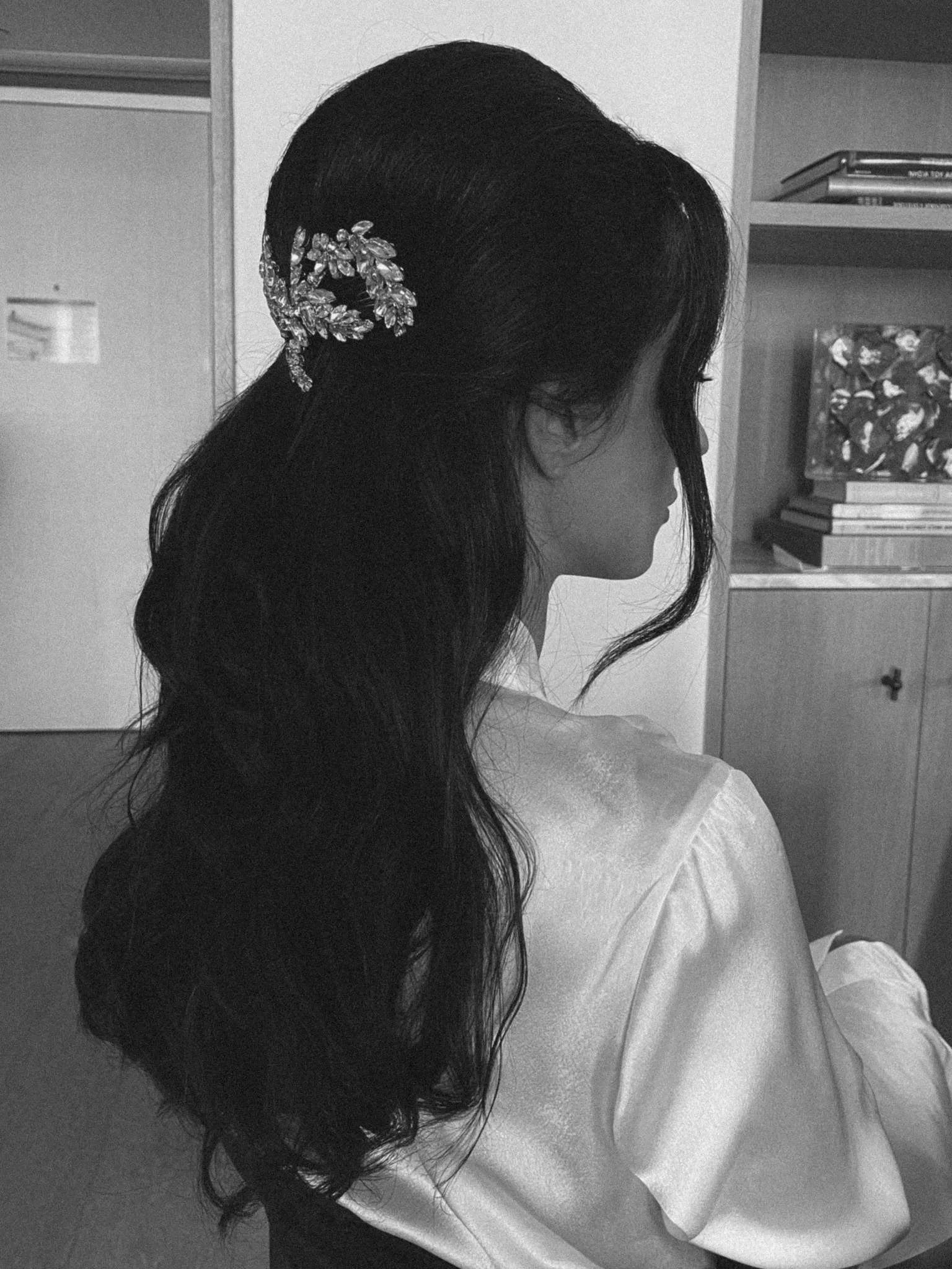 Side profile of a woman with long dark hair styled with a jeweled hairclip, sitting indoors.