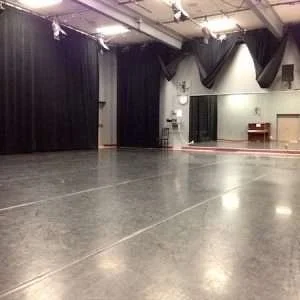 Empty performance stage with black curtains, lighting, and a polished floor.