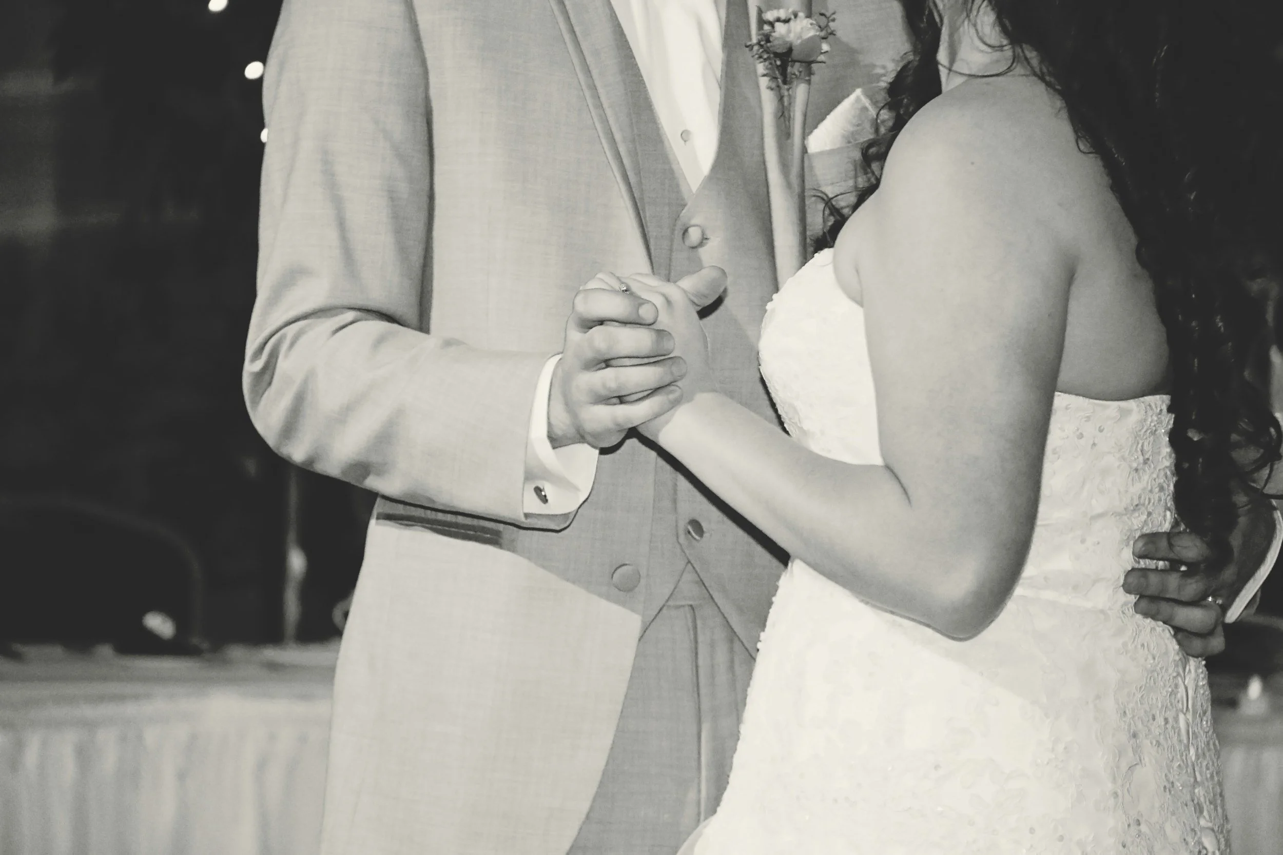 A black and white photo of a bride and groom holding hands during their wedding ceremony.