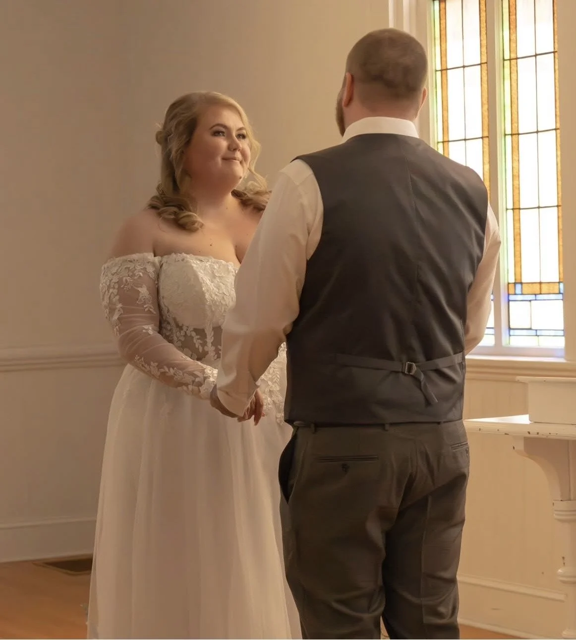 A bride and groom holding hands during a wedding ceremony inside a church with stained glass windows.