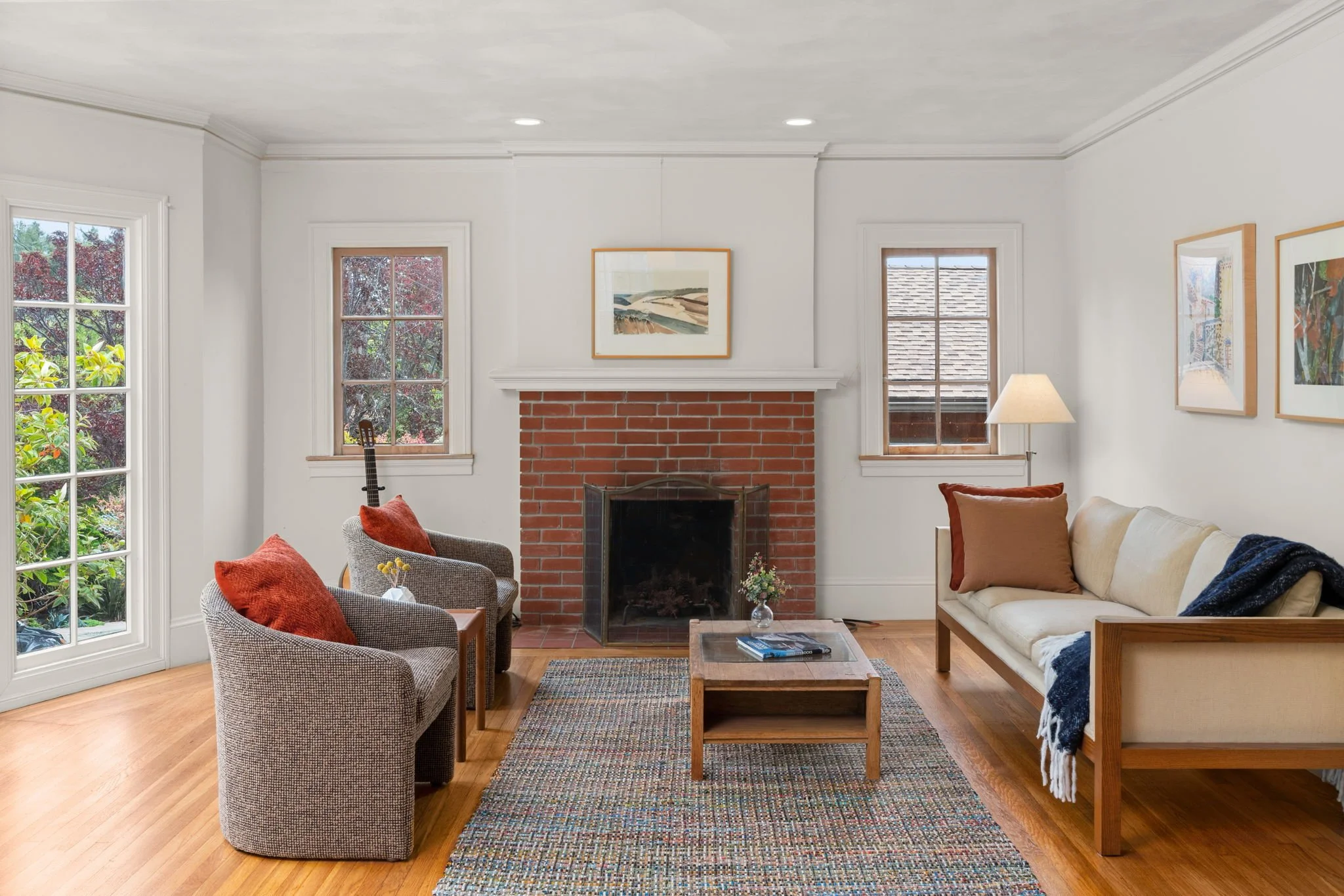 Living room with two gray armchairs, a cream-colored sofa, a brick fireplace, and wooden flooring.