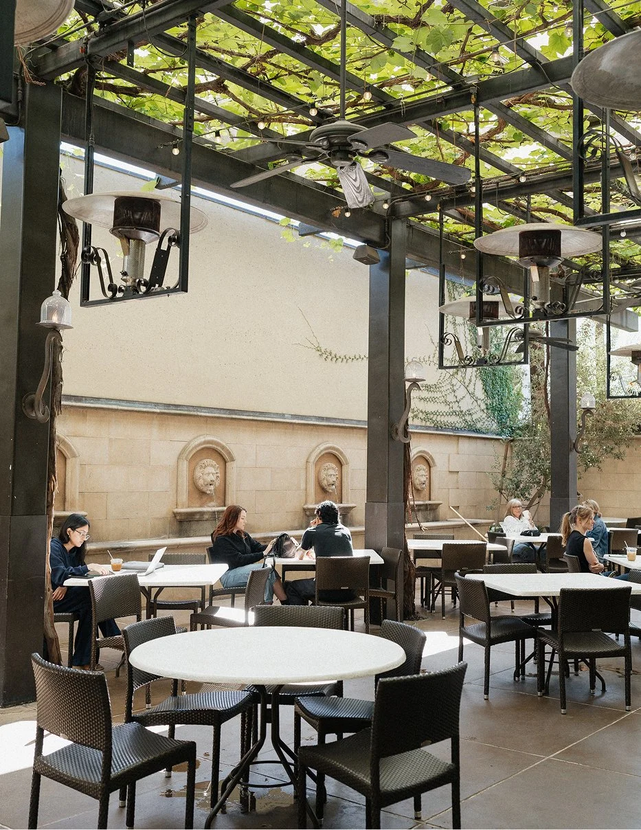 Sunlit outdoor patio seating area at Galletto Ristorante in Modesto with pergola covered in greenery and stone wall accents
