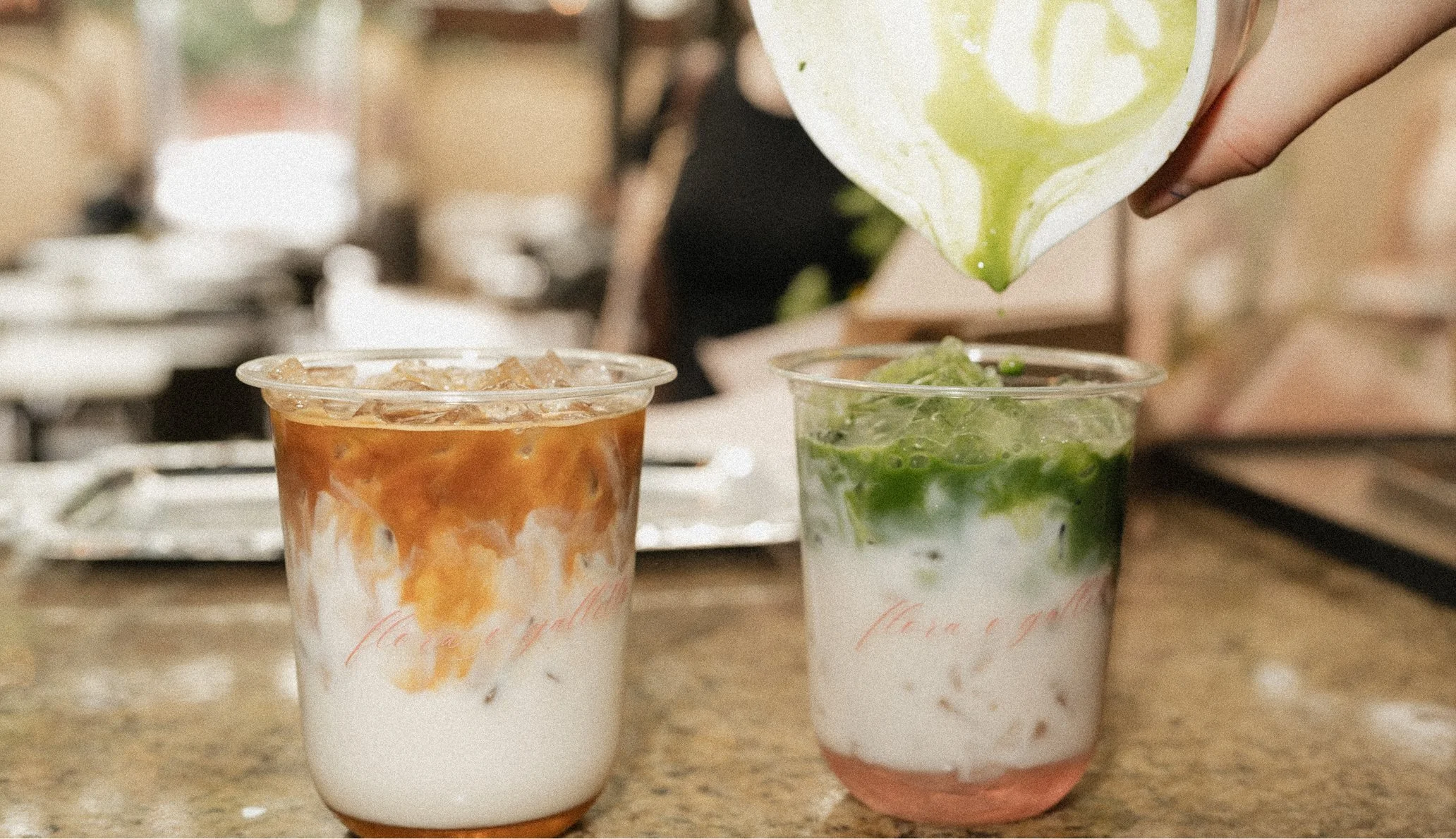 Two iced beverages in clear cups, one with a caramel and cream mixture and the other with a green leafy mint or herb topping, on a kitchen counter.
