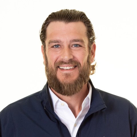 Headshot of a smiling man with a beard and slicked-back hair, wearing a dark jacket and white shirt, against a plain white background.