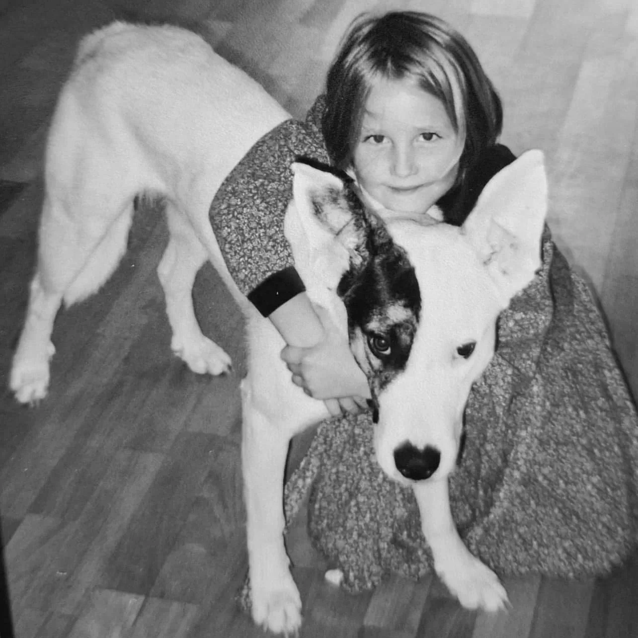 Ein lachendes Mädchen umarmt einen großen Hund, wahrscheinlich ein Siberian Husky, in einem Innenraum. Schwarz-weiß-Foto.